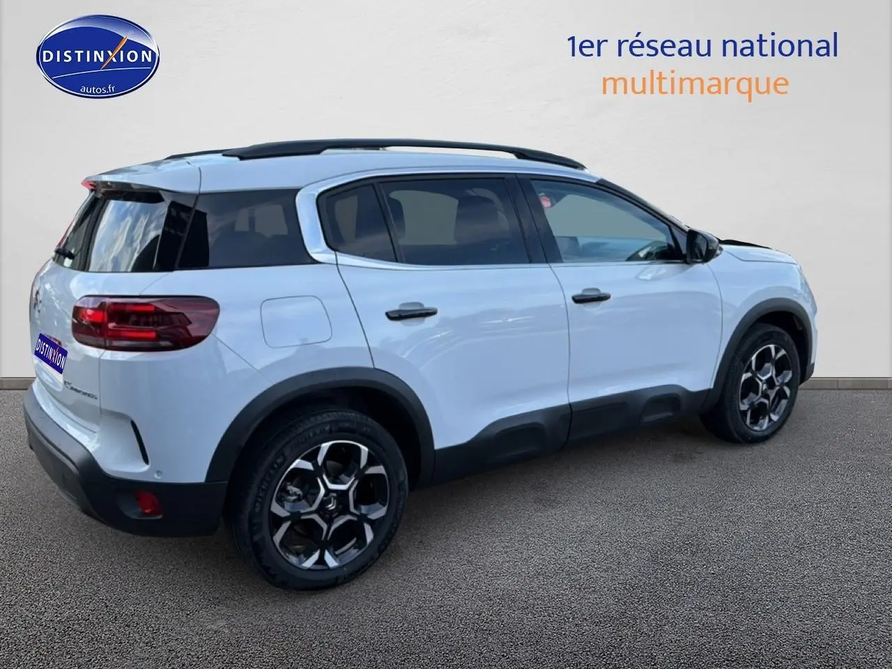 Vue 3/4 arrière droite d'un Citroën C5 Aircross blanc avec barres de toit et jantes alu noires et argentées.