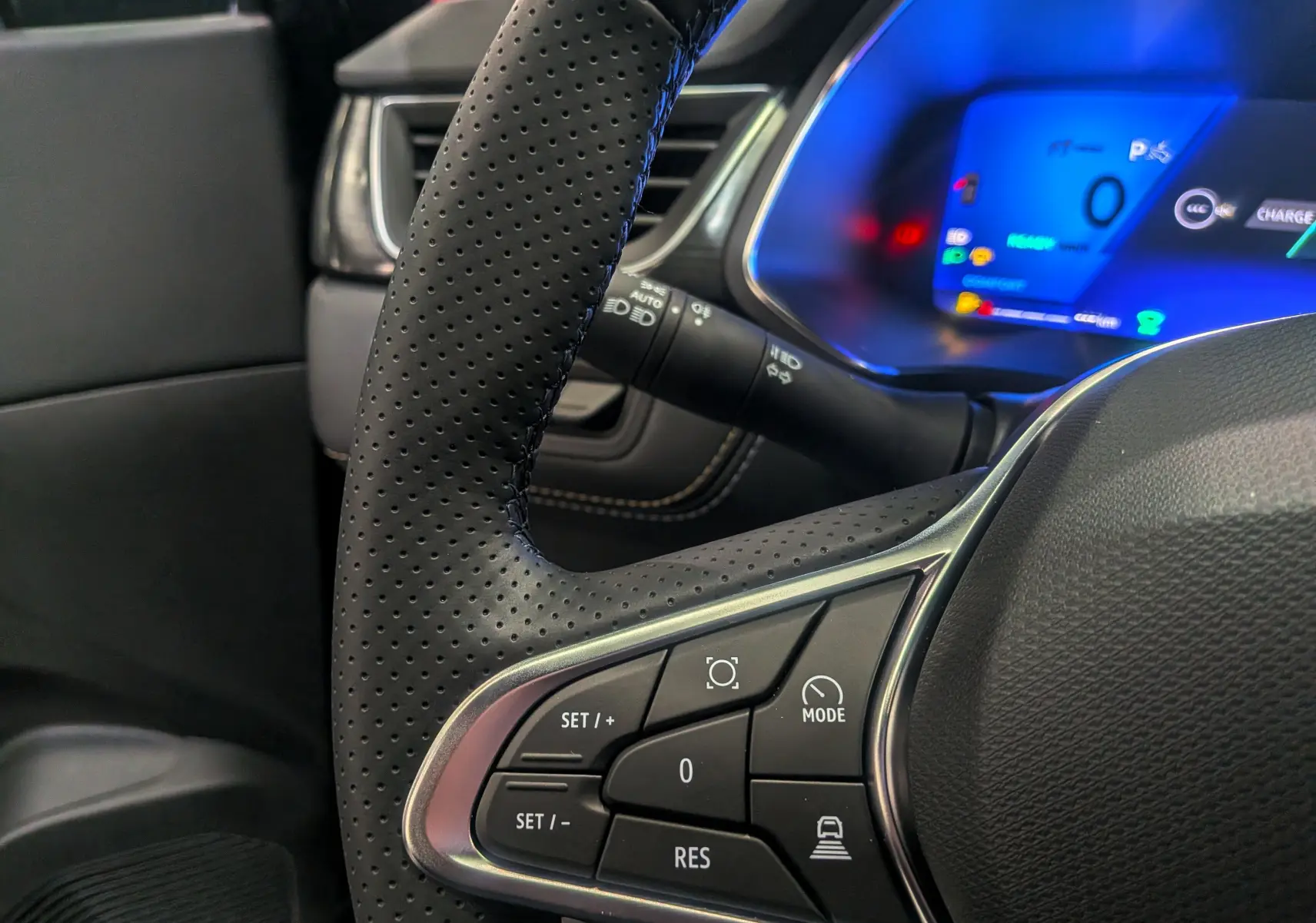 Gros plan sur le volant perforé et les commandes multifonctions d’un Renault Symbioz E-Tech noir étoilé, tableau de bord numérique bleu visible.