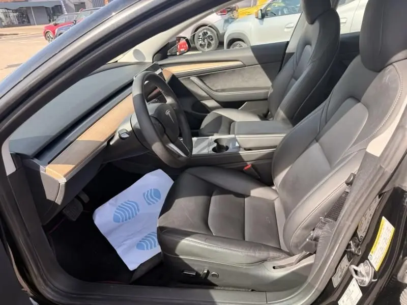Vue intérieure côté conducteur de la Tesla Model 3 Standard RWD Plus 2022 noire, sièges cuir et tableau de bord bois.