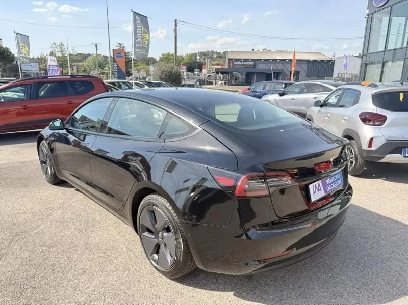 Tesla Model 3 Standard RWD Plus noir vue 3/4 arrière droit, stationnée en extérieur sur un parking lumineux.
