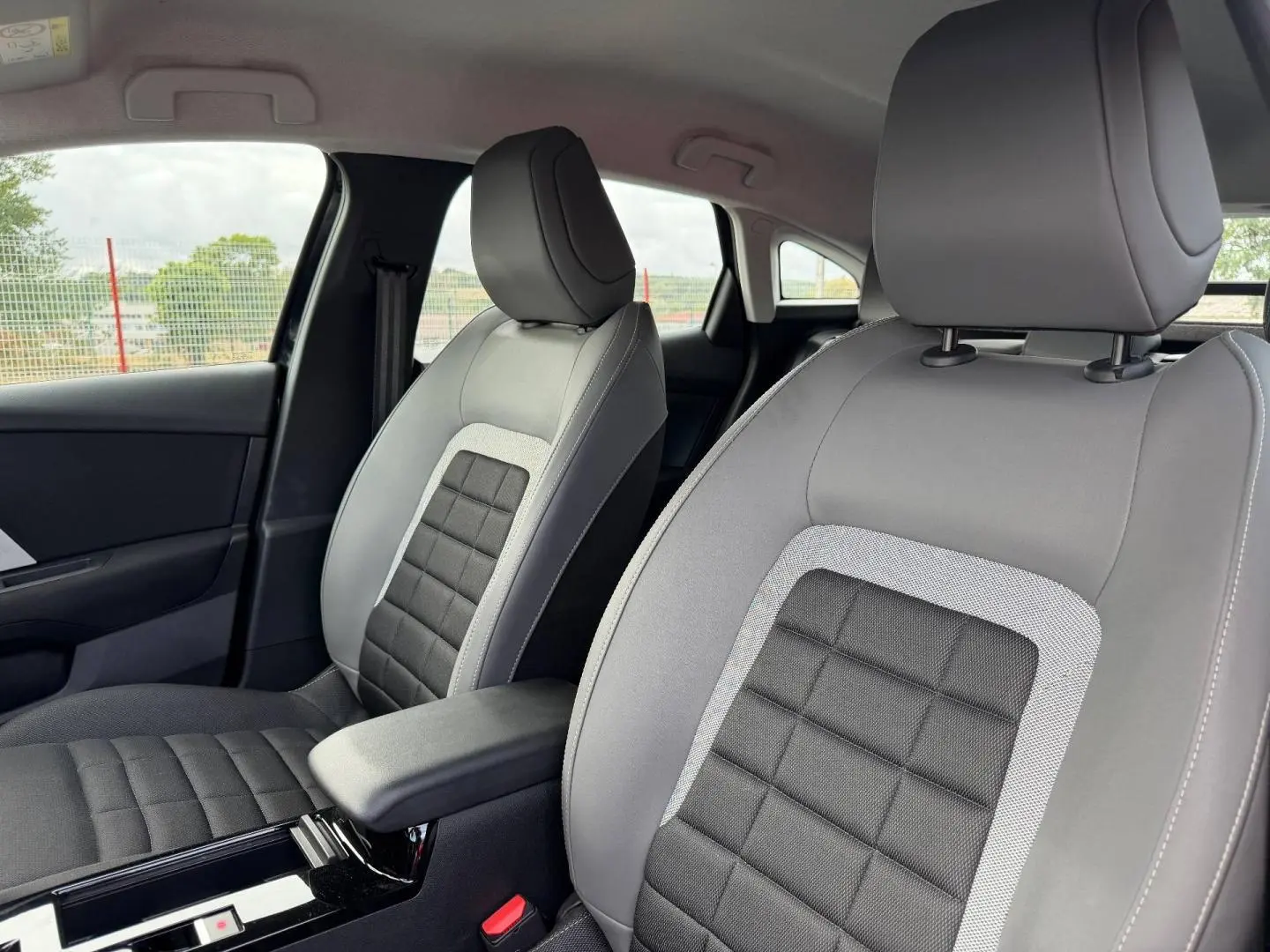 Gros plan sur les sièges avant gris et noirs avec accoudoir central de la Citroën C4 1.2 Hybride 2025.