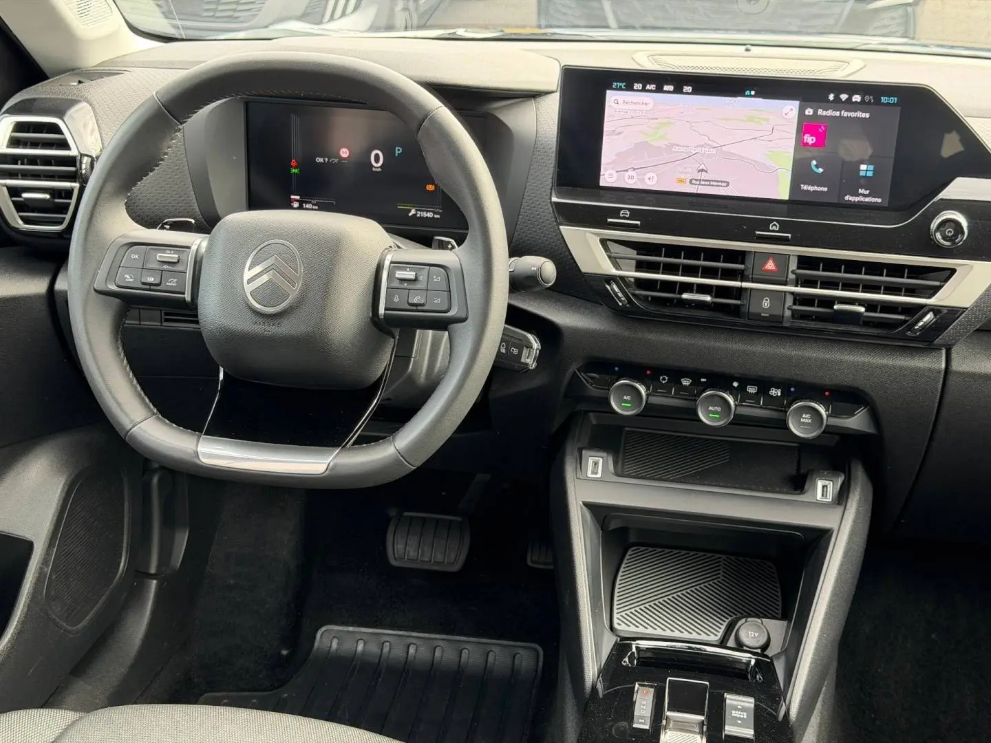 Vue intérieure avant du tableau de bord noir d'une Citroën C4 1.2 Hybride avec écran tactile et volant cuir.