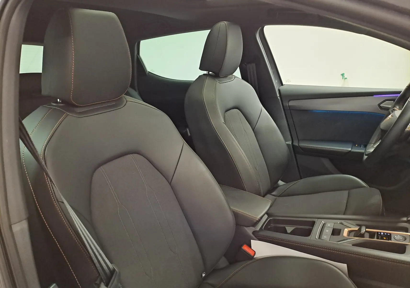 Vue intérieure côté conducteur et passager avant de la CUPRA Leon 1.5 eTSI 150 DSG7 avec sièges noirs et surpiqûres cuivrées.