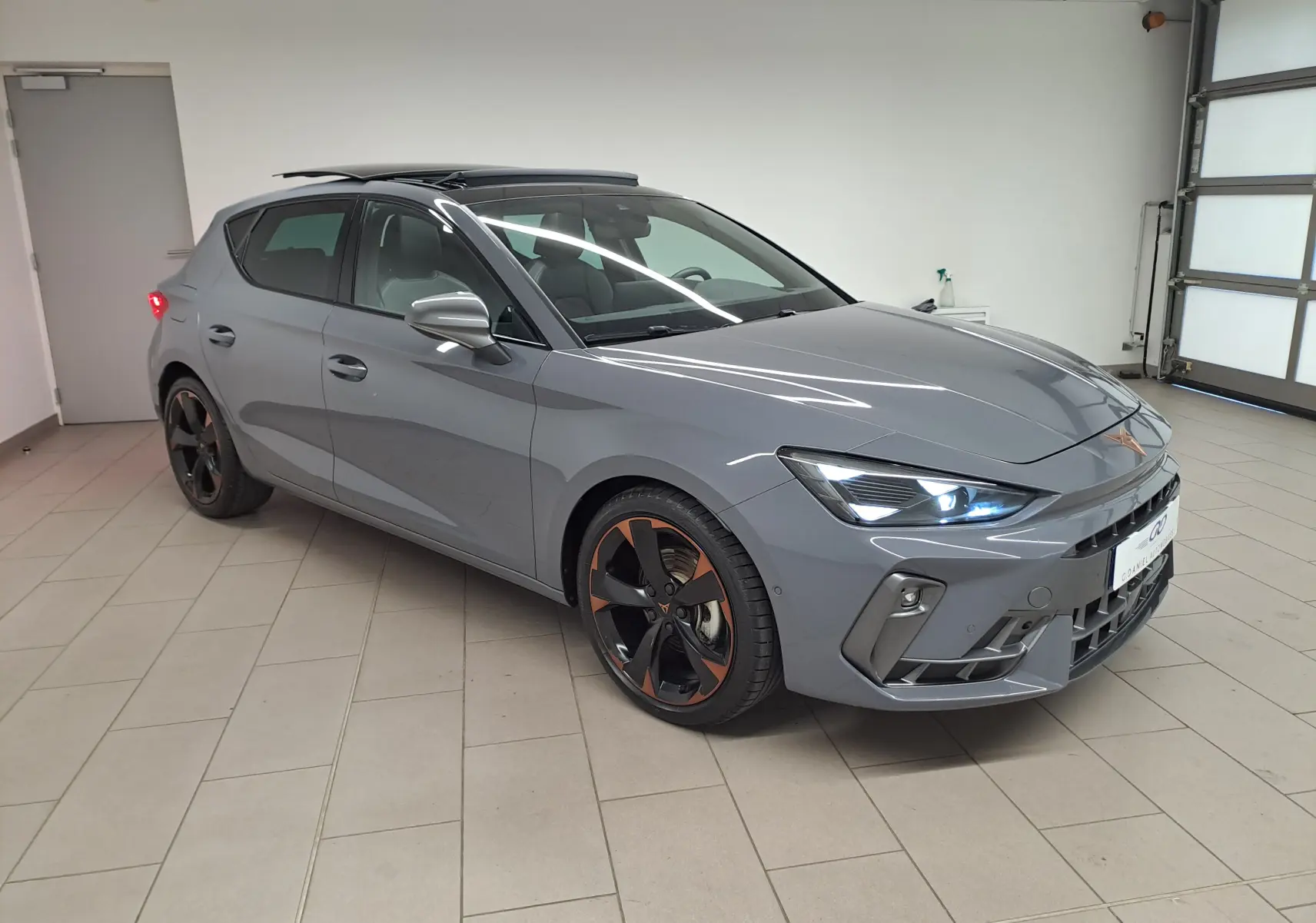 Vue 3/4 avant droit d'une CUPRA Leon 2025 gris graphène avec toit ouvrant panoramique et jantes cuivrées 18 pouces.