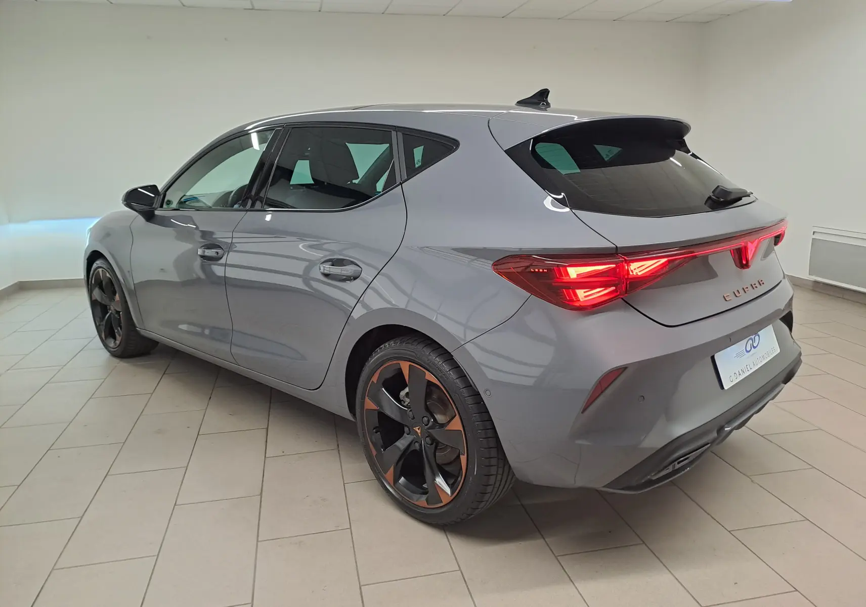 Vue 3/4 arrière droite d'une CUPRA Leon 2025 gris Graphène avec jantes cuivrées et toit ouvrant panoramique.