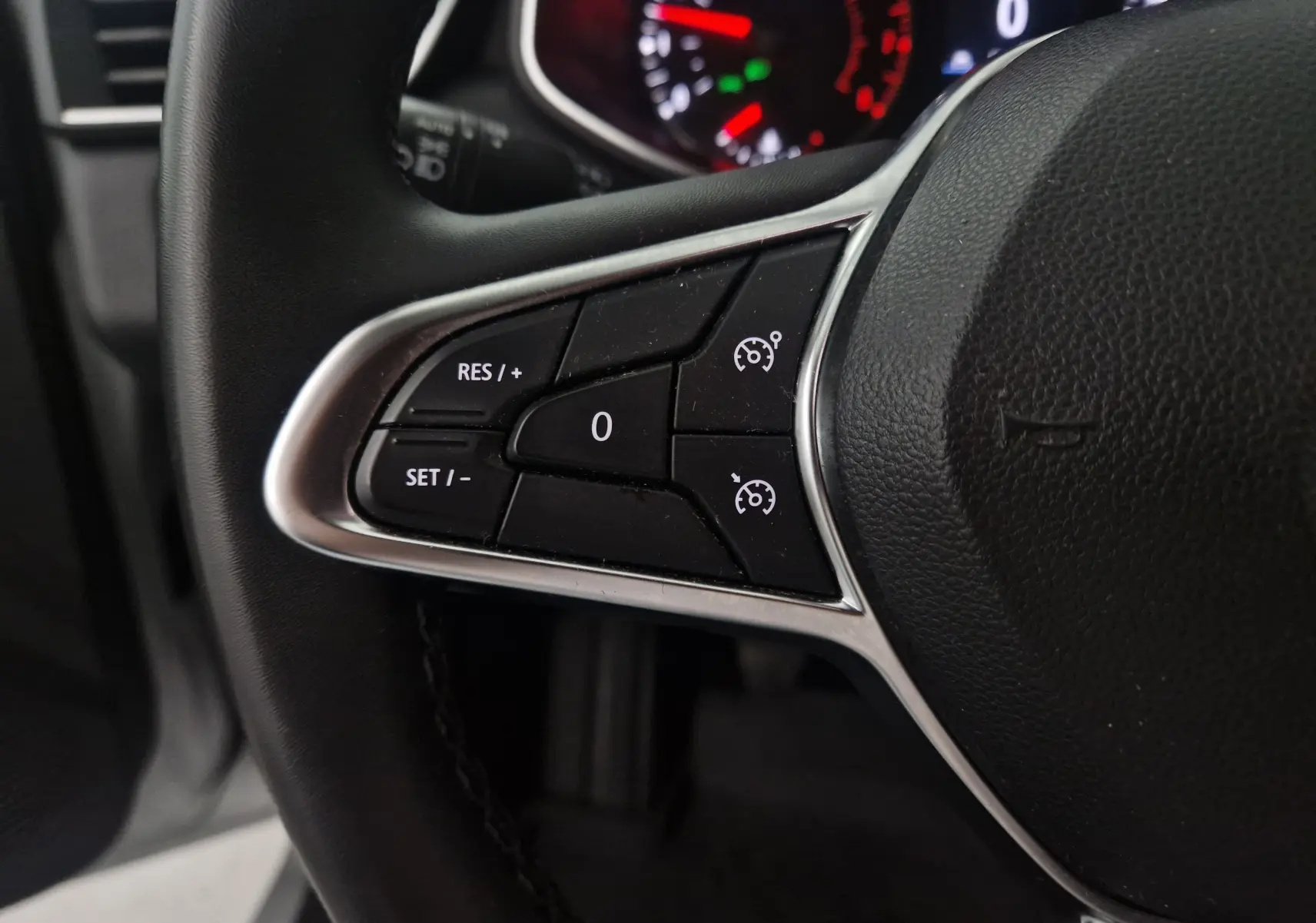 Gros plan sur les commandes de régulateur de vitesse à gauche du volant d'une Renault Clio V gris platine, tableau de bord en arrière-plan.