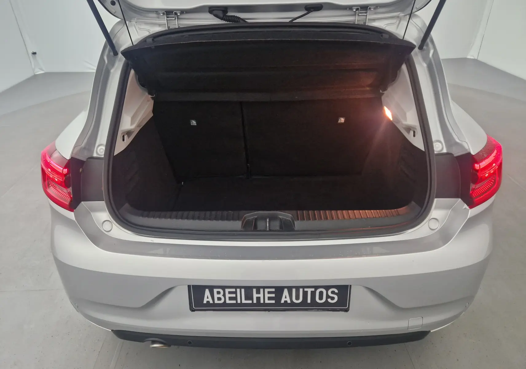Coffre ouvert vu de l'arrière d'une Renault Clio V gris platine, montrant l'espace de chargement vide et l'éclairage intérieur.