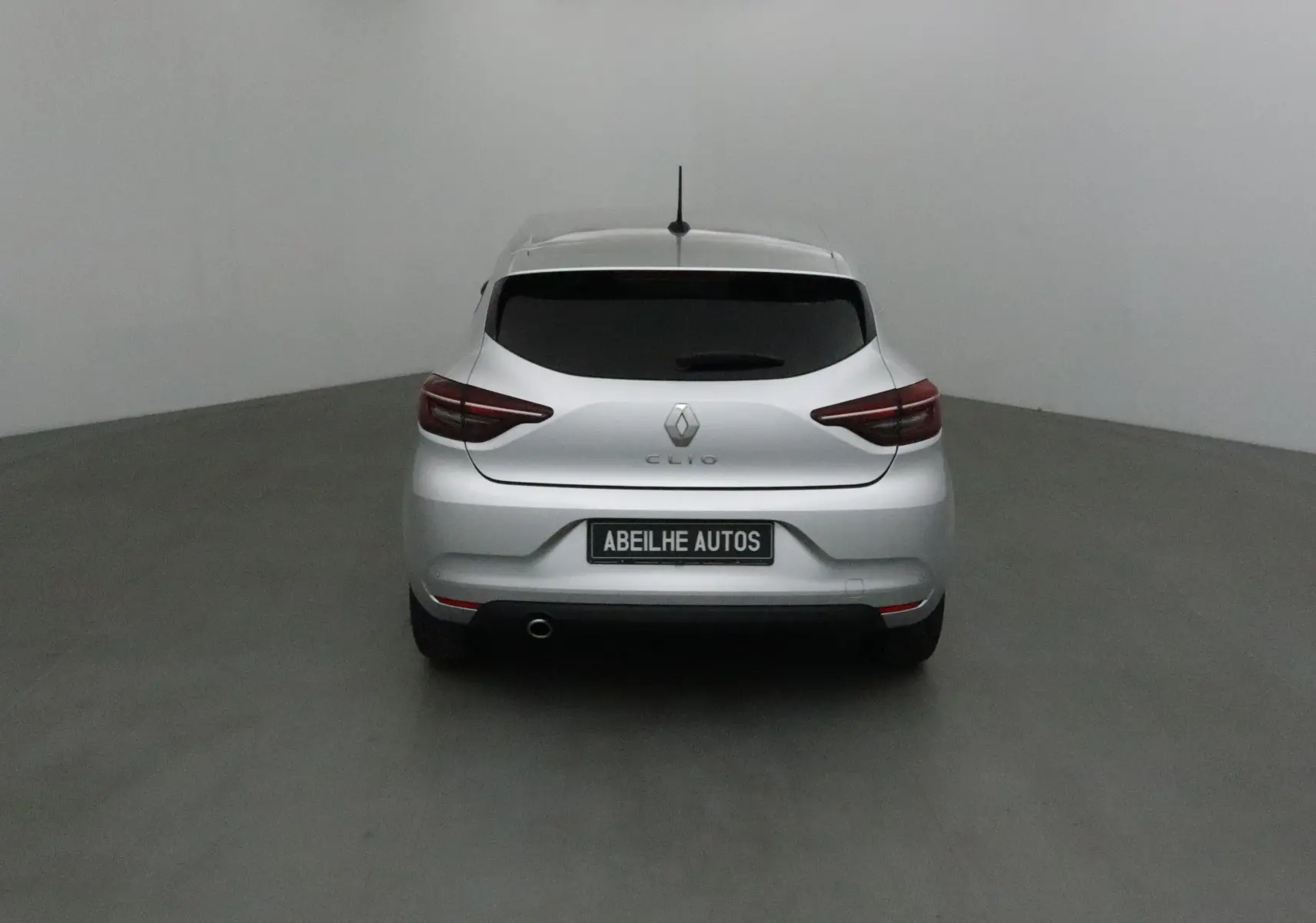 Vue arrière d'une Renault Clio V gris platine avec vitres teintées et plaque Abeilhe Autos dans un studio.