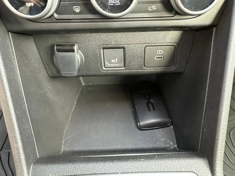 Gros plan sur la console centrale noire d'une Dacia Sandero 2025 avec prise USB-C, bouton de siège chauffant et prise 12V.