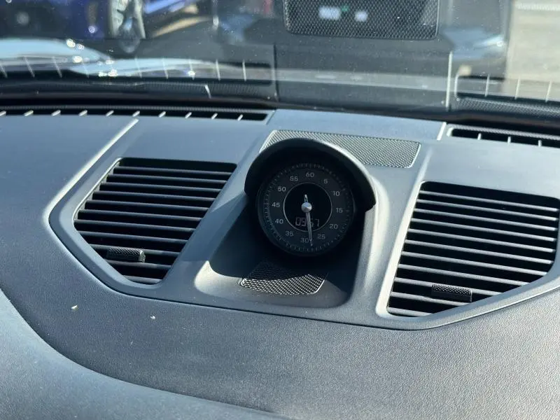 Gros plan sur l'horloge centrale noire du tableau de bord de la Porsche 911 Turbo S 2020, entourée de grilles d'aération.