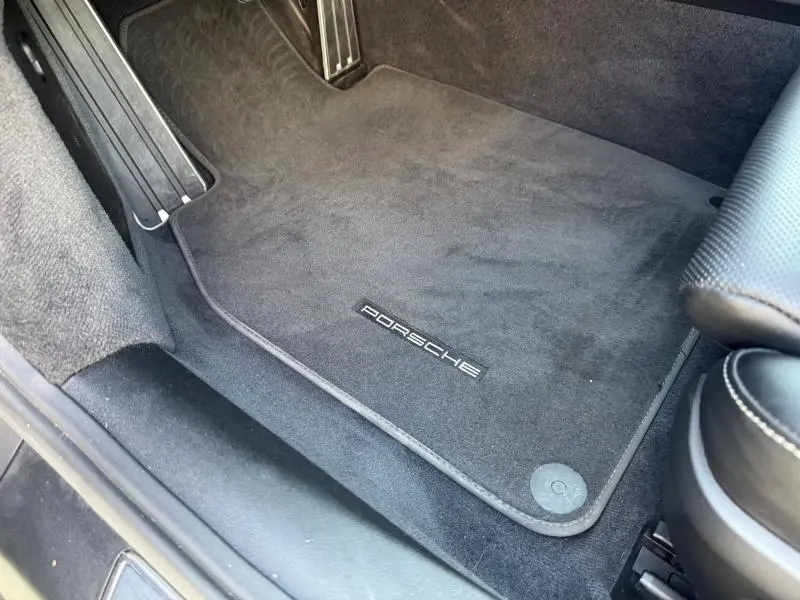 Vue intérieure côté conducteur montrant le tapis de sol noir avec logo Porsche et pédales en aluminium.