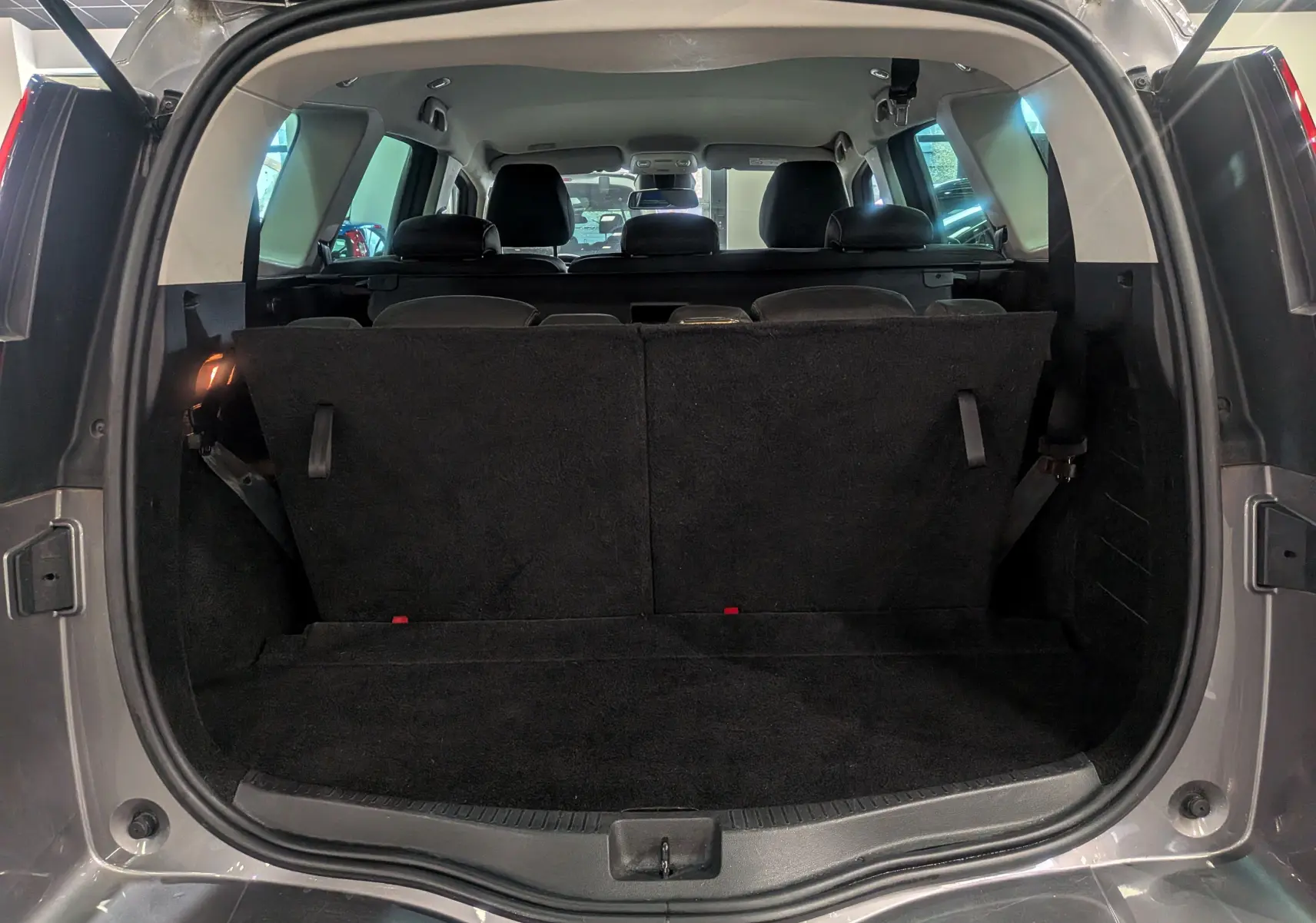 Coffre ouvert vu de l'arrière d'un Renault Grand Scénic IV gris Cassiopé avec banquette arrière relevée et intérieur sombre.