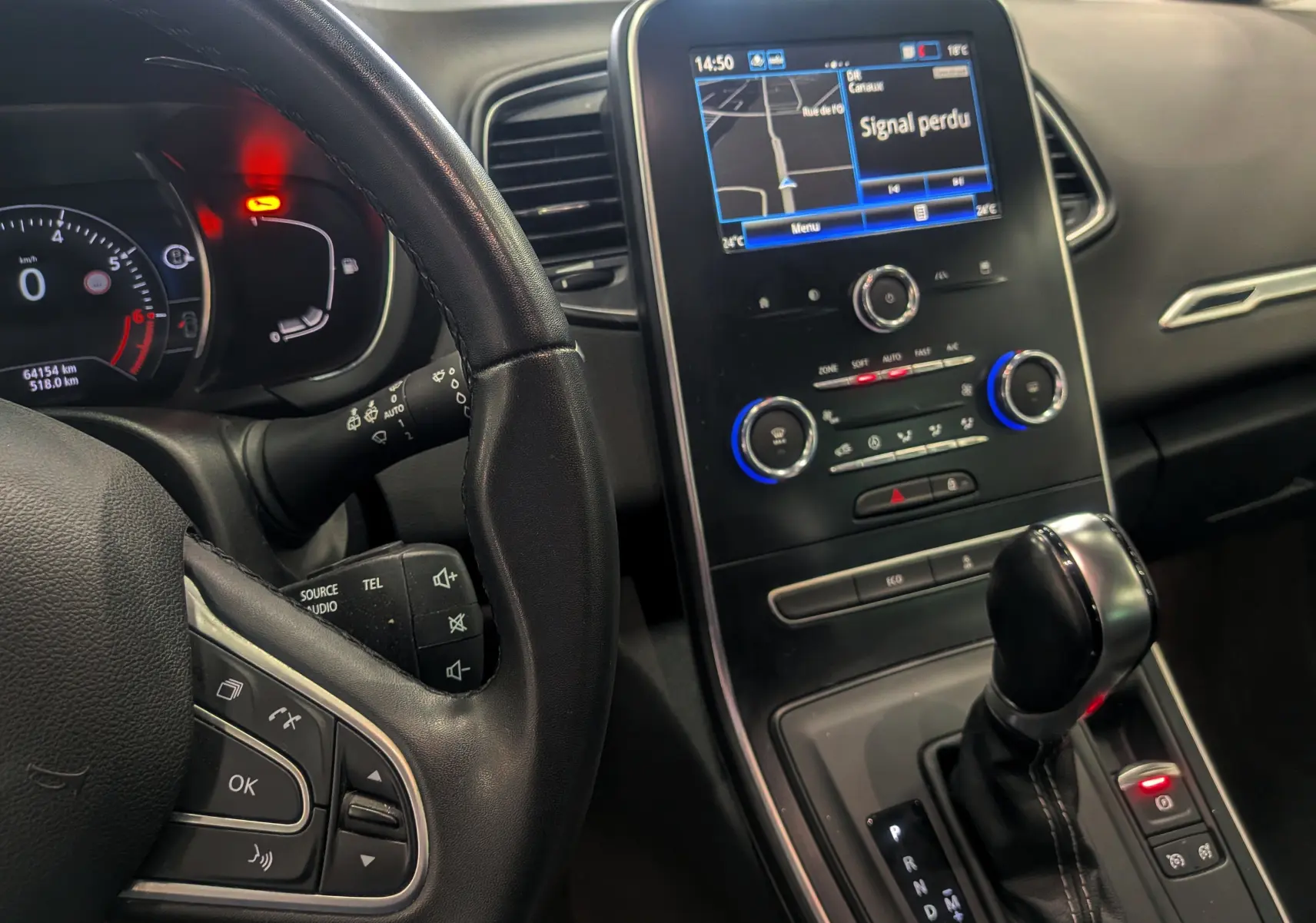 Vue intérieure centrée sur le tableau de bord et levier de vitesse d’un Renault Grand Scenic IV gris Cassiopé, avec écran tactile allumé.
