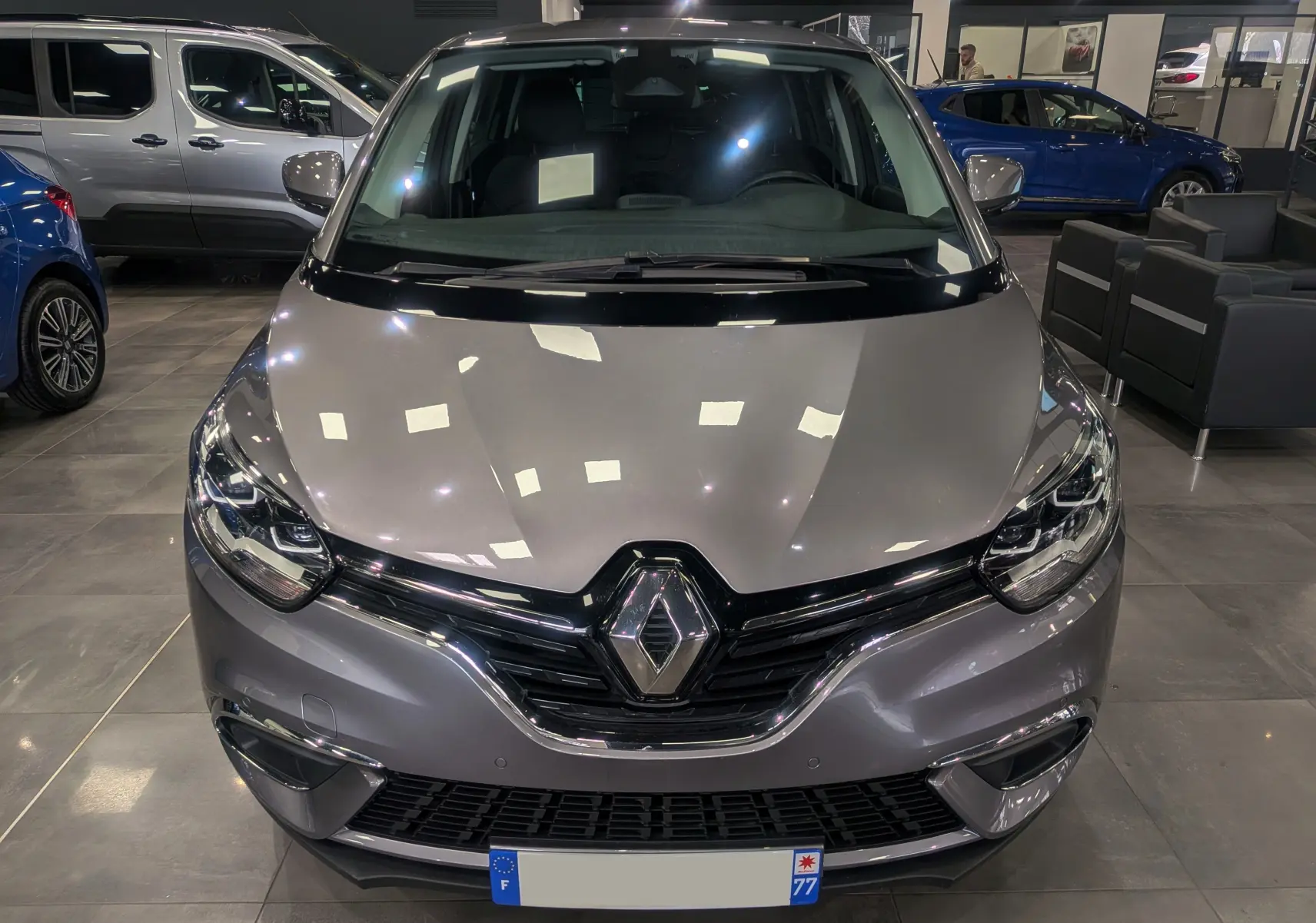 Vue avant d'un Renault Grand Scénic IV gris Cassiopé, avec calandre noire et logo Renault bien visible en showroom.