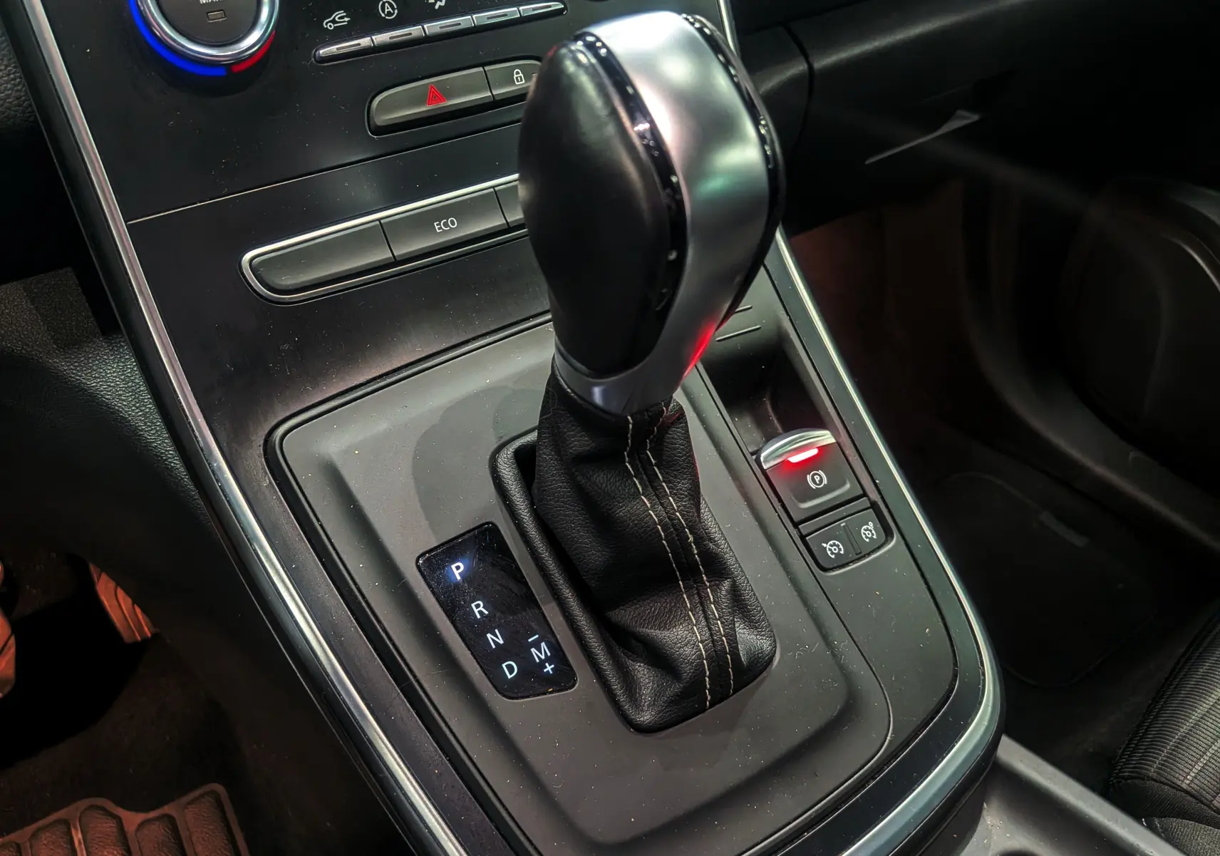 Gros plan sur le levier de vitesses automatique noir et argenté du Renault Grand Scenic IV TCe 140, intérieur sombre.
