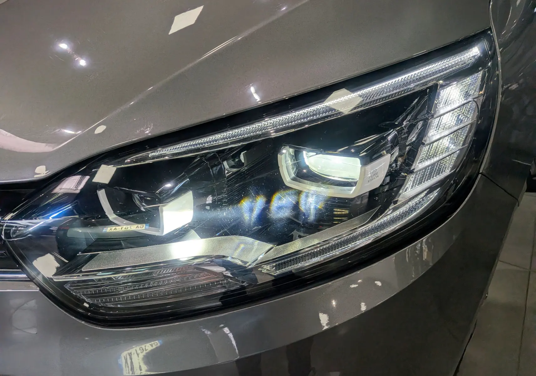 Gros plan sur le phare avant droit du Renault Grand Scenic IV gris Cassiopé, mettant en valeur son design LED moderne.