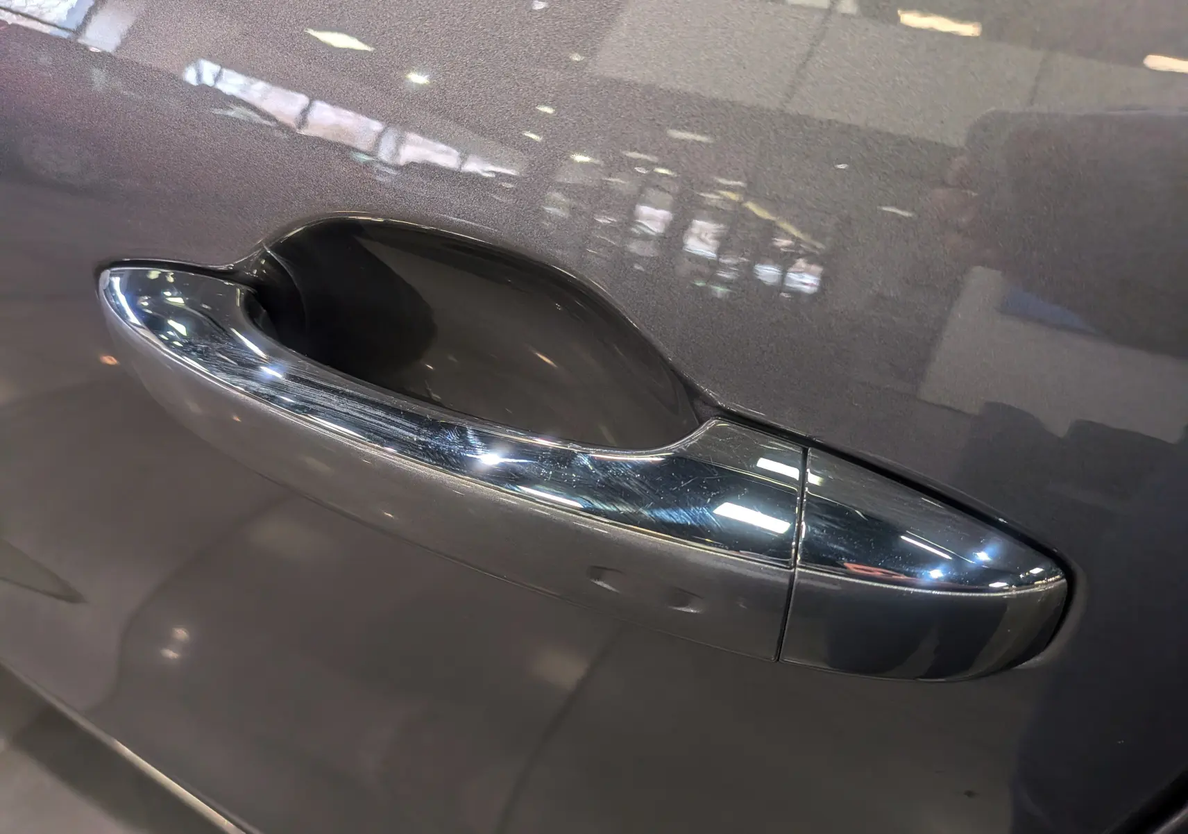 Poignée de porte chromée sur la portière côté gauche d’un Renault Grand Scenic IV gris Cassiopé, reflet intérieur visible.