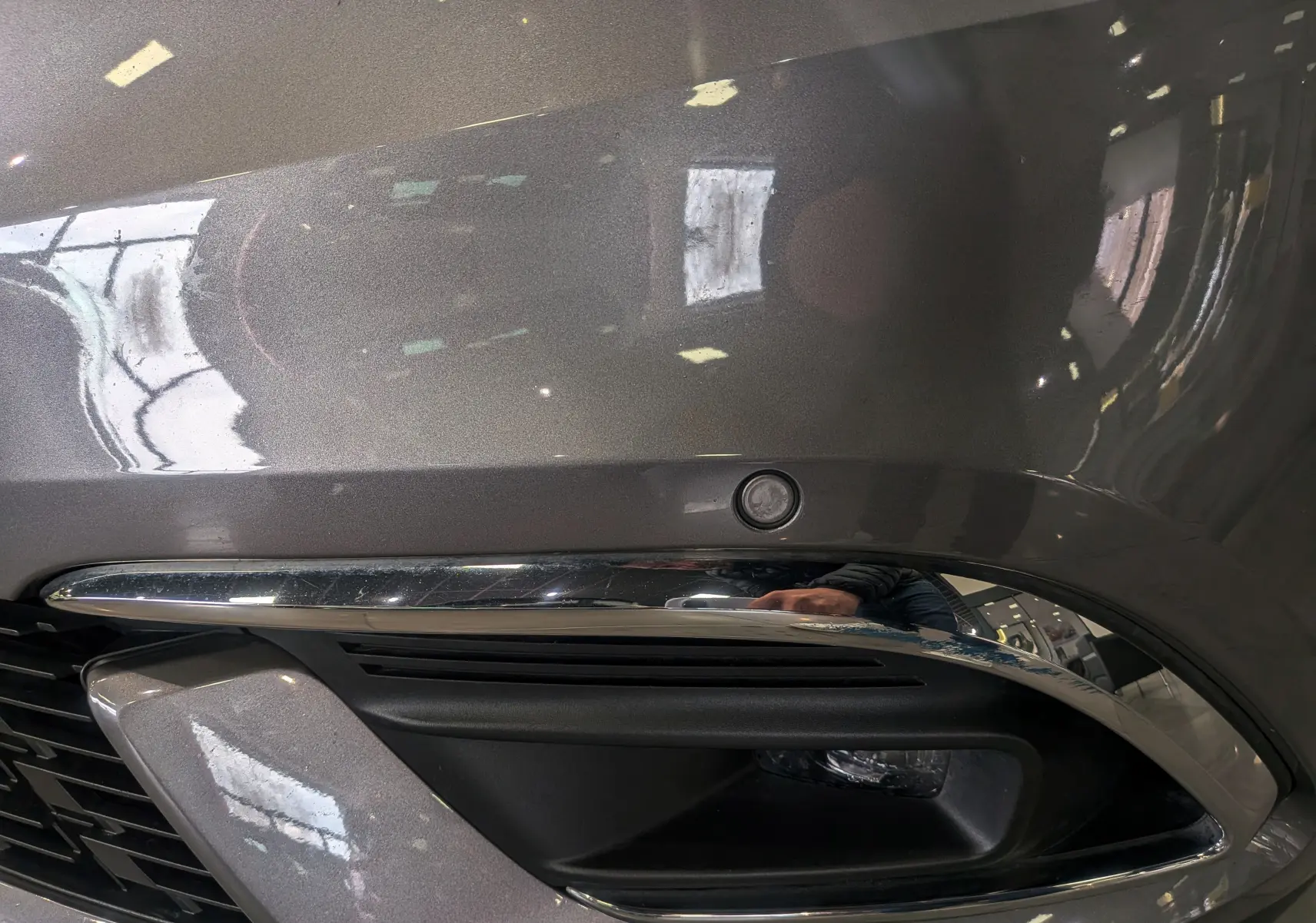 Gros plan sur le pare-chocs avant gris Cassiopé du Renault Grand Scénic IV avec capteur de stationnement et insert chromé.