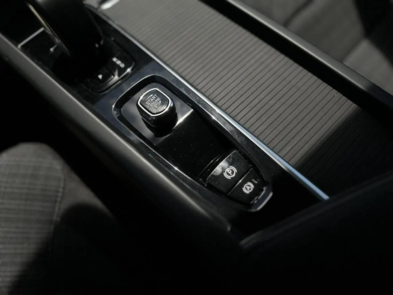 Gros plan sur la console centrale noire du Volvo S60 2024, avec bouton Start/Stop et frein de parking électronique.