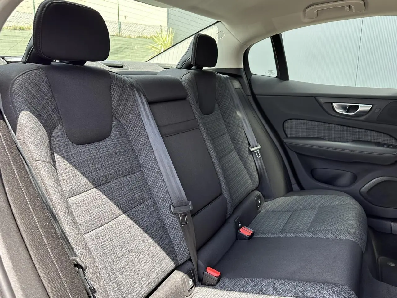 Vue intérieure côté droit des sièges arrière en tissu gris à motifs de la Volvo S60 2024, avec ceinture de sécurité visible.