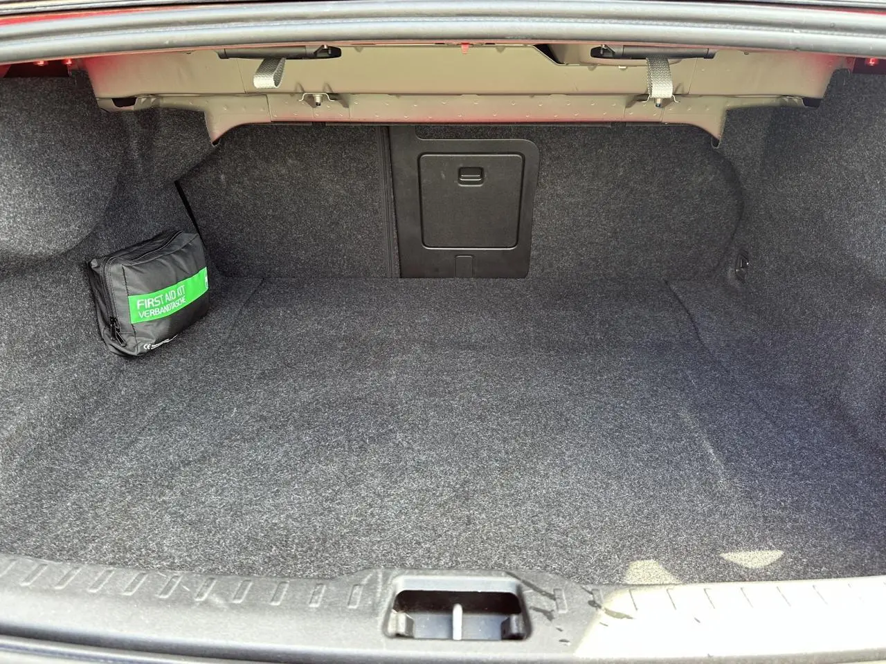 Coffre ouvert d'une Volvo S60 B4 2024 Rouge Fusion, montrant un espace de rangement avec trappe centrale et trousse de secours.