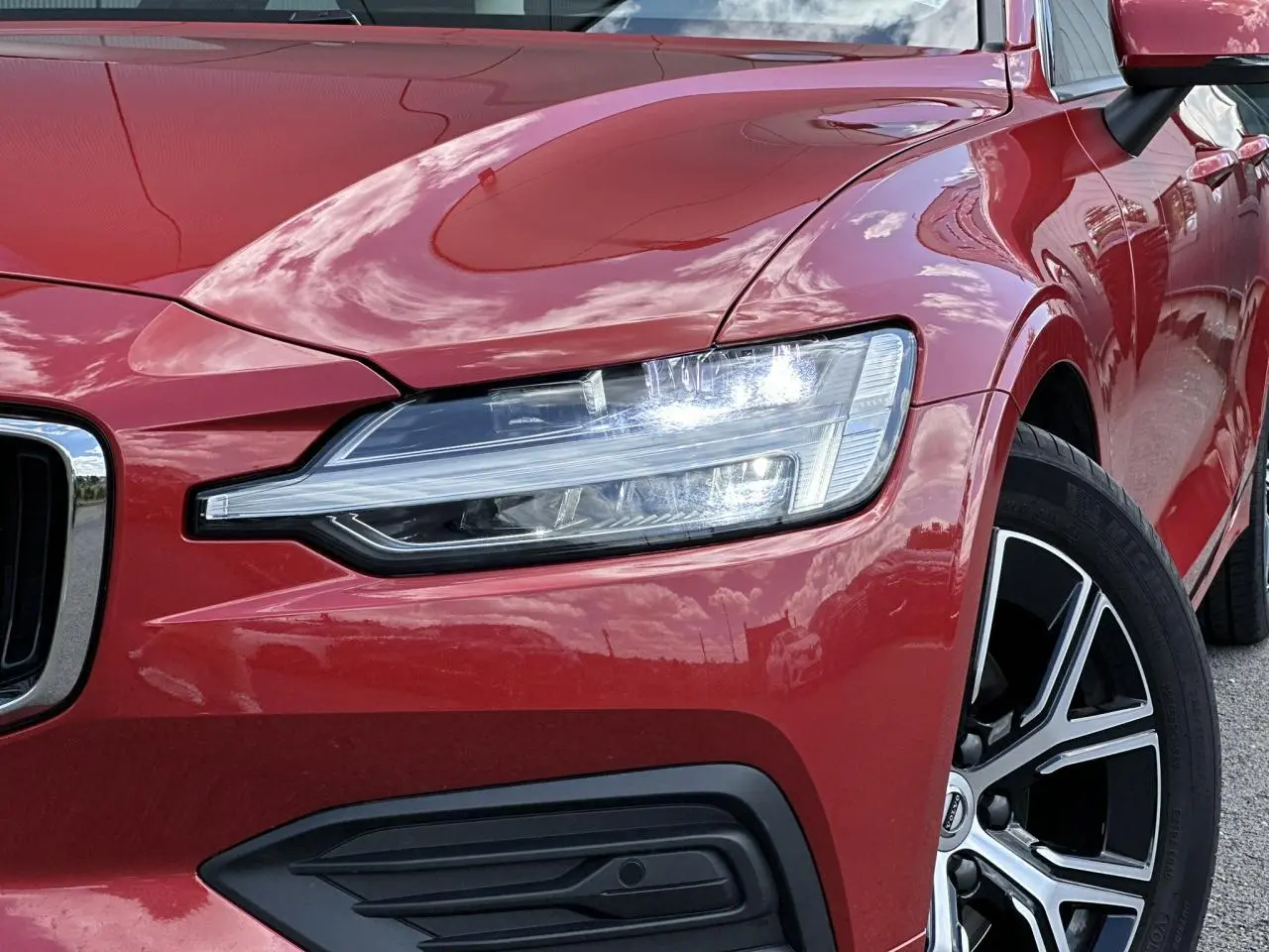 Gros plan sur l'avant droit de la Volvo S60 rouge Fusion 2024, mettant en valeur le phare LED et la jante alliage noire diamant.