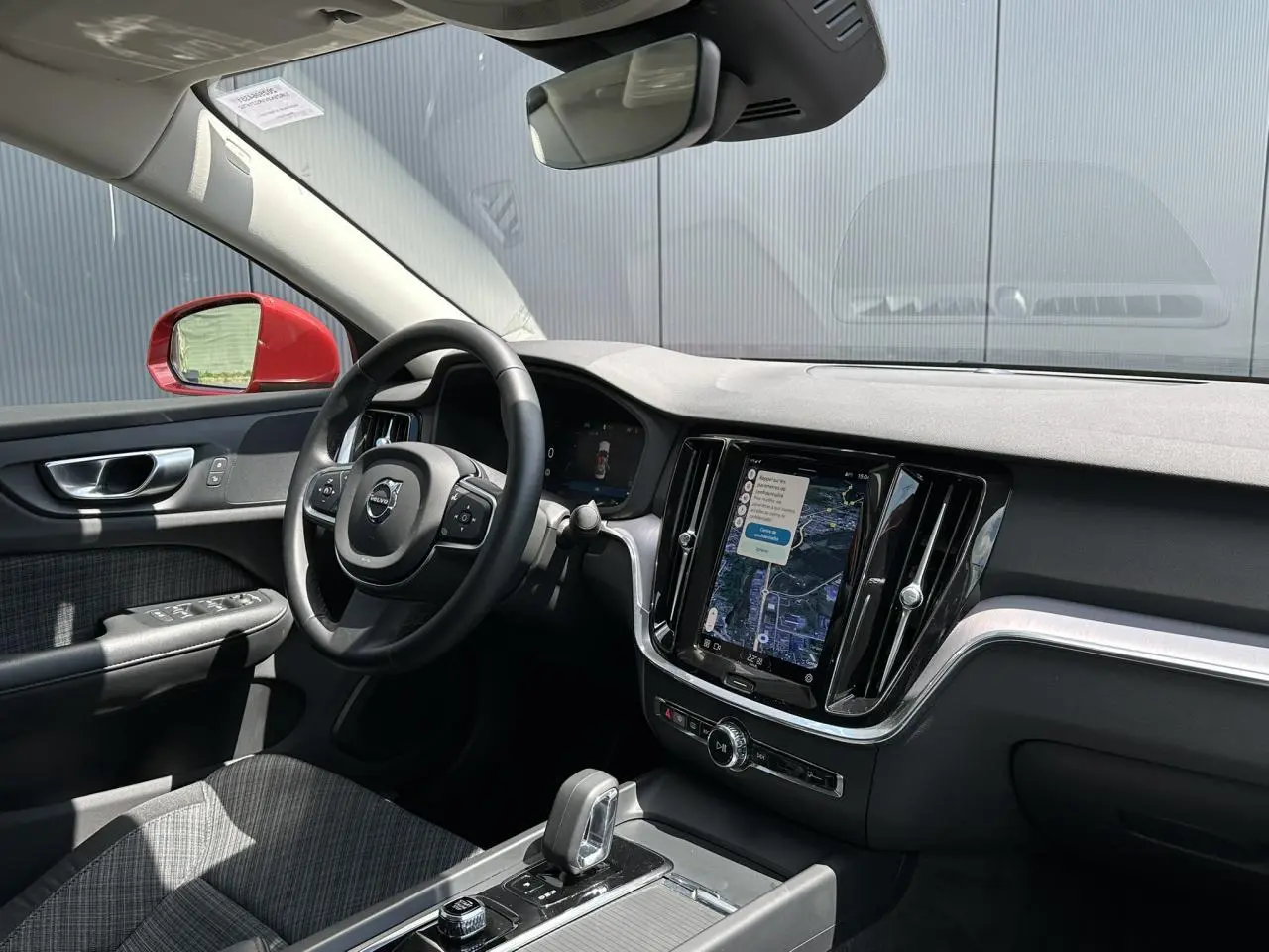 Vue intérieure côté conducteur de la Volvo S60 rouge Fusion 2024, avec tableau de bord et écran tactile GPS visible.