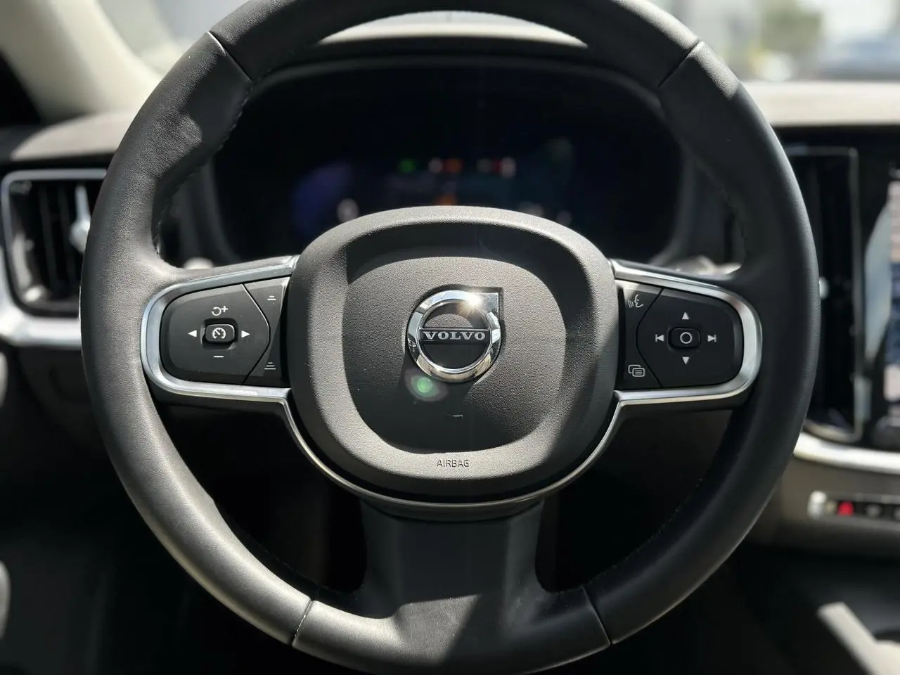 Vue rapprochée du volant noir de la Volvo S60 2024 avec commandes intégrées et logo central brillant.