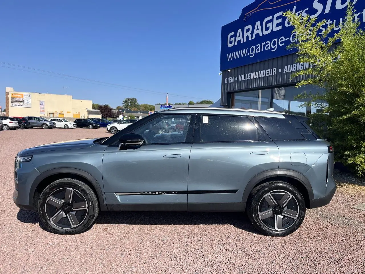 Vue de profil côté gauche du SUV JAECOO J7 gris olive, avec vitres arrière surteintées et jantes modernes noires.