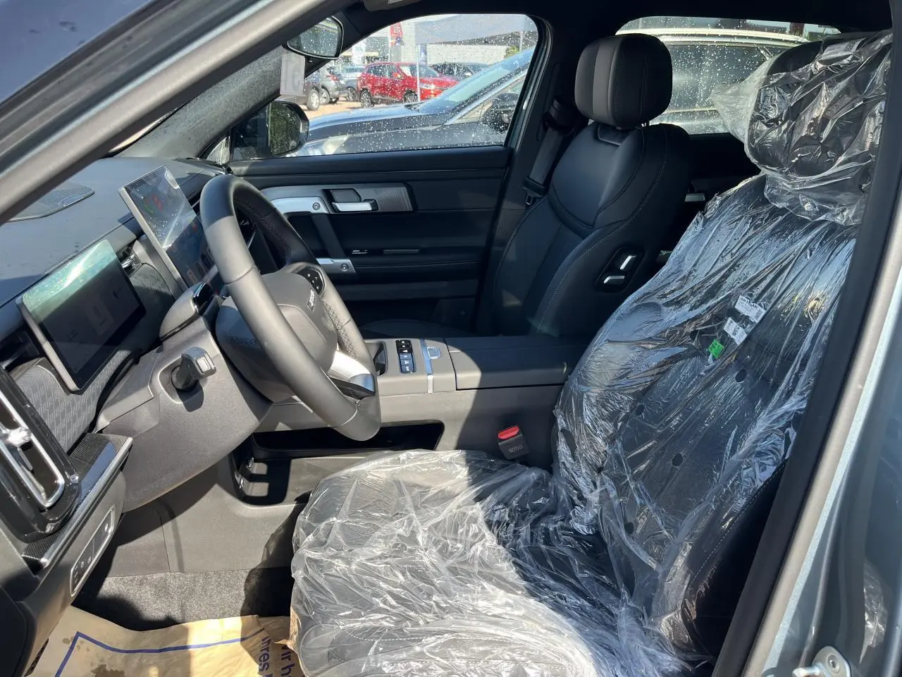 Vue intérieure côté conducteur du JAECOO J7 1.5 SHS-P gris olive, sièges noirs protégés par film plastique.