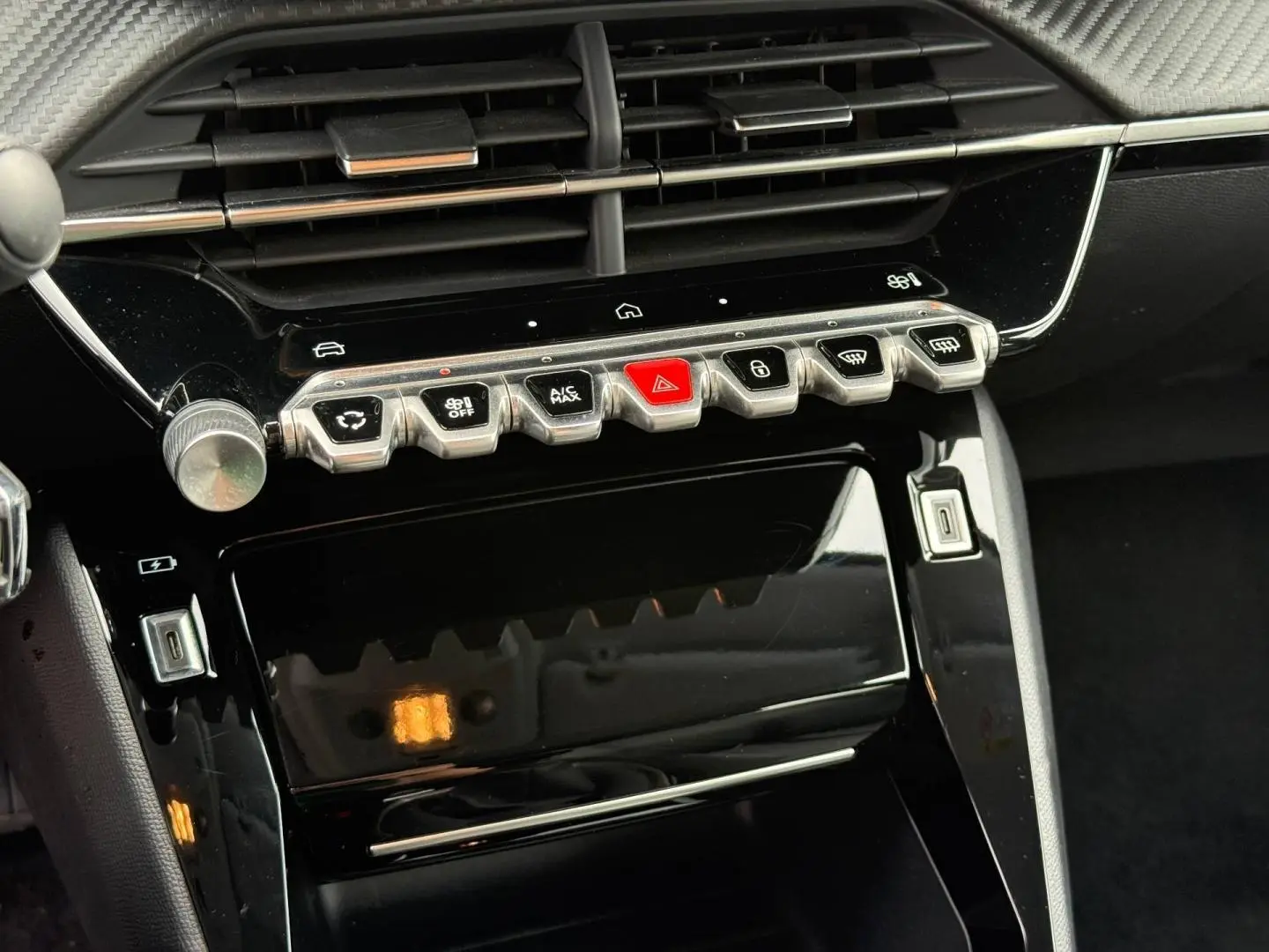 Vue rapprochée de la console centrale noire brillante de la Peugeot 208 1.2 100ch Allure avec ses commandes tactiles et boutons métalliques.