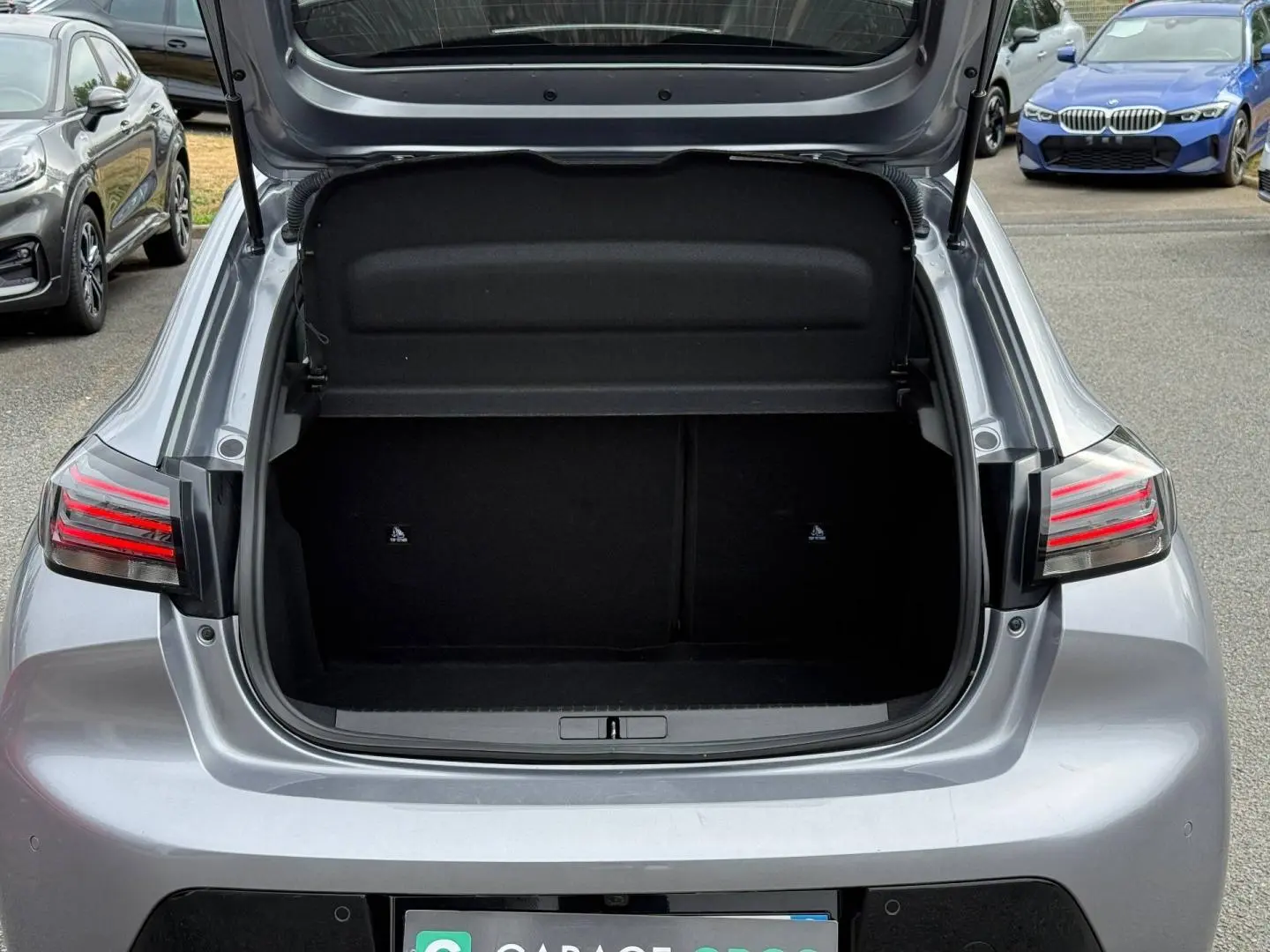 Coffre ouvert d’une Peugeot 208 gris Artense vue de l’arrière, avec feux arrière LED allumés.