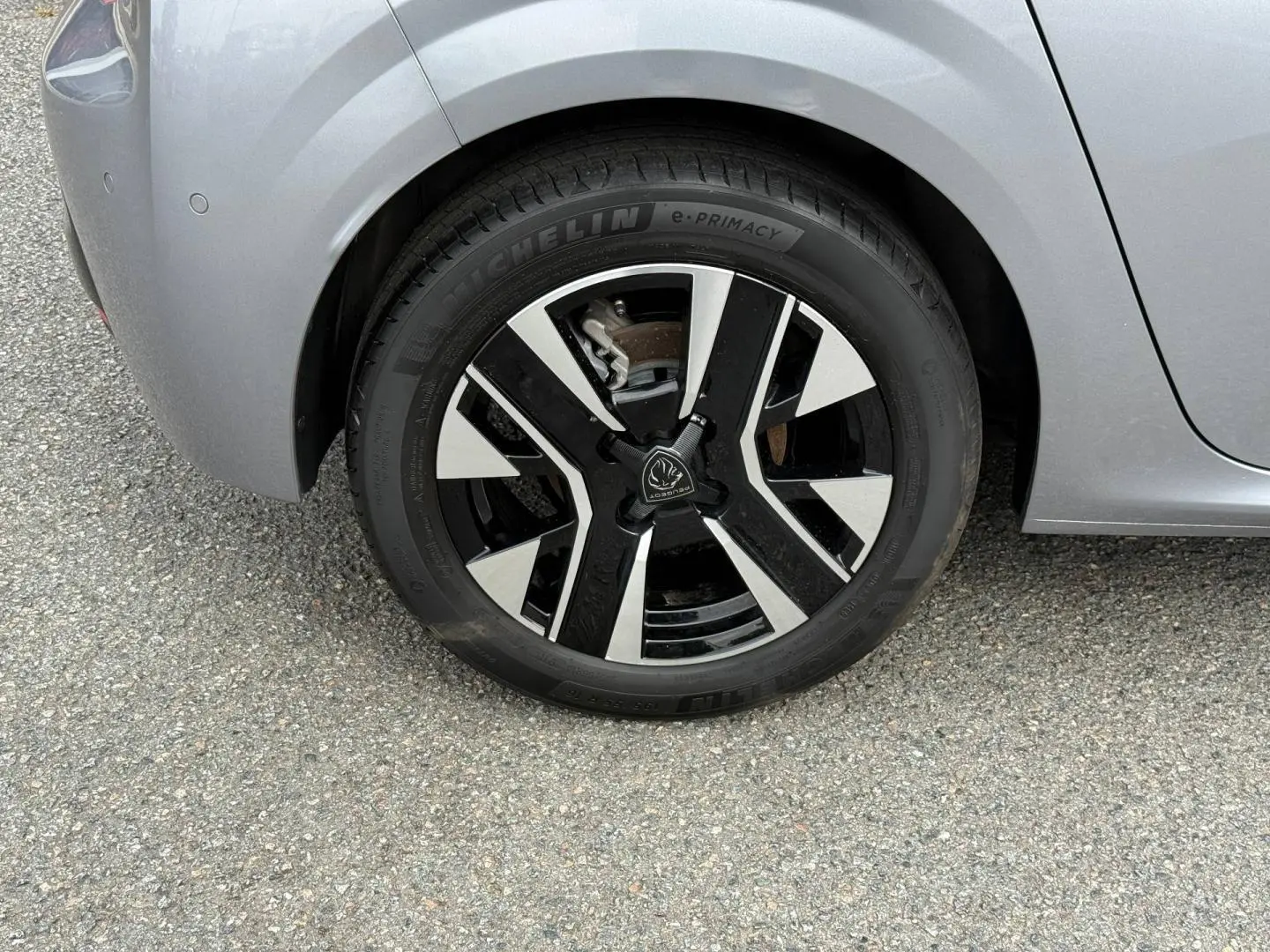 Gros plan sur la roue avant gauche d'une Peugeot 208 gris Artense avec jante alu noire et argentée.