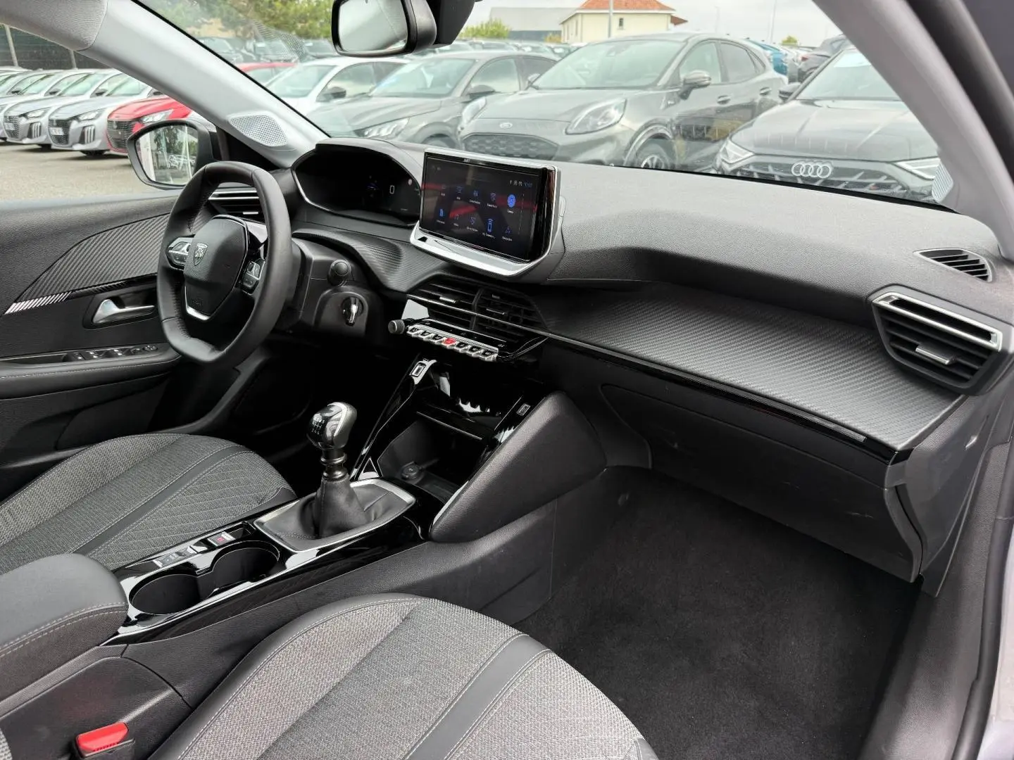 Intérieur avant droit de la Peugeot 208 1.2 100ch gris Artense, avec tableau de bord moderne et écran tactile central.