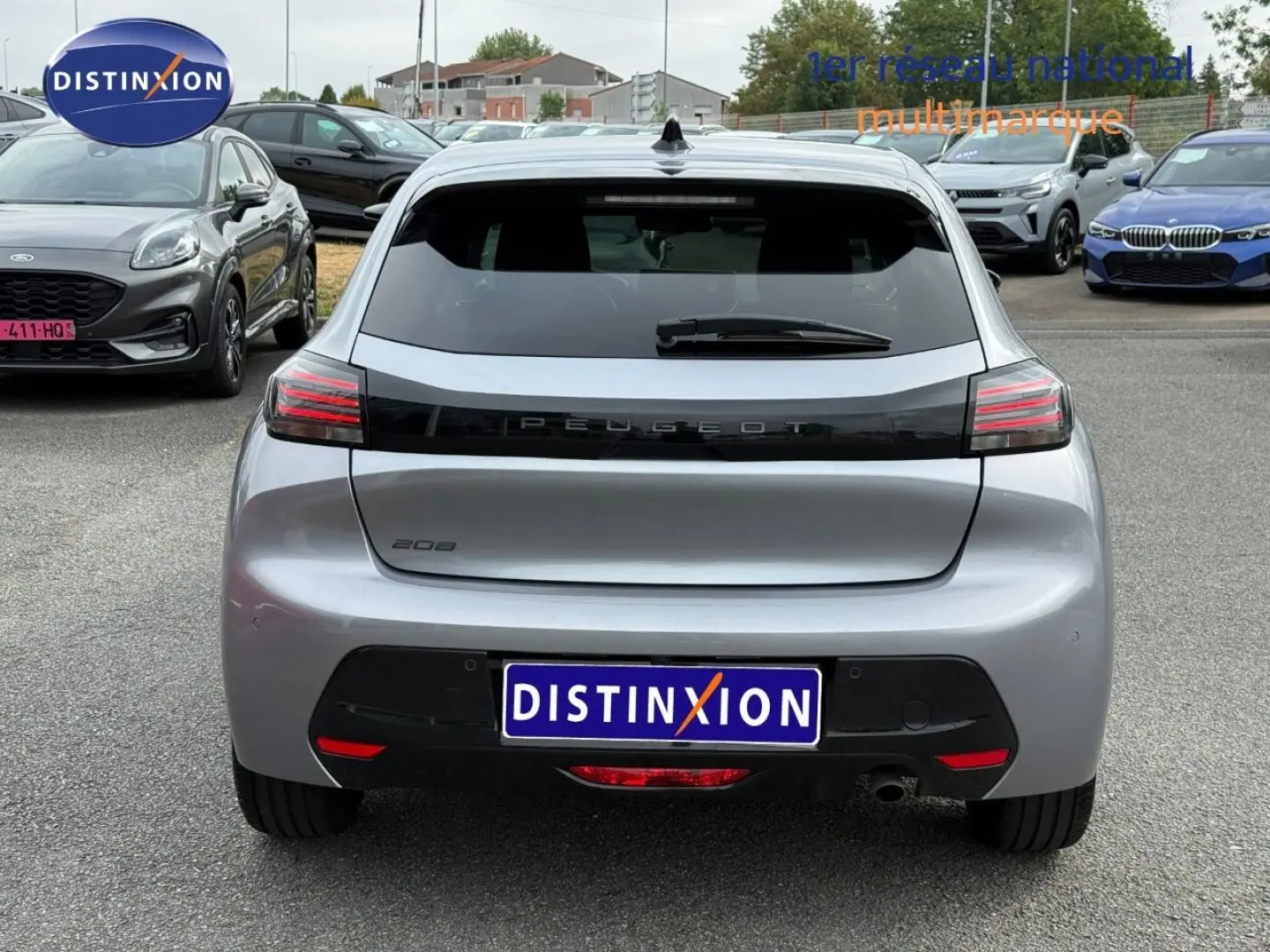 Vue arrière d'une Peugeot 208 gris Artense avec feux arrière LED et lunette arrière surteintée, en extérieur sur parking.