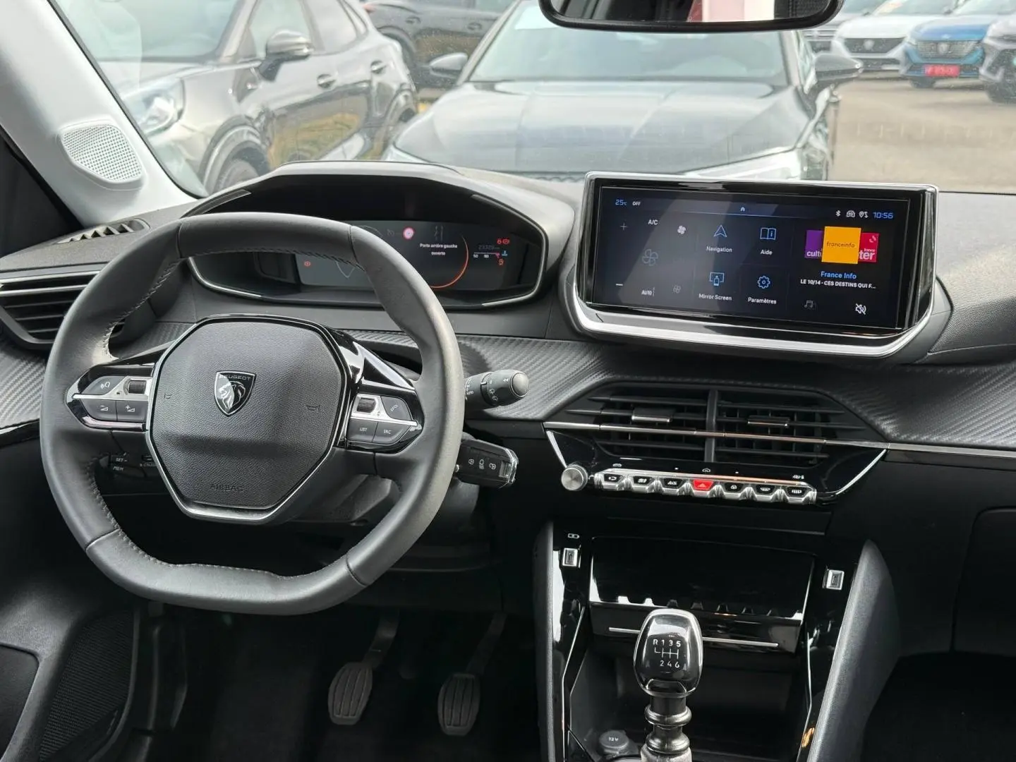 Vue intérieure avant de la Peugeot 208 gris Artense, volant compact, écran tactile et levier de vitesses manuel visibles.