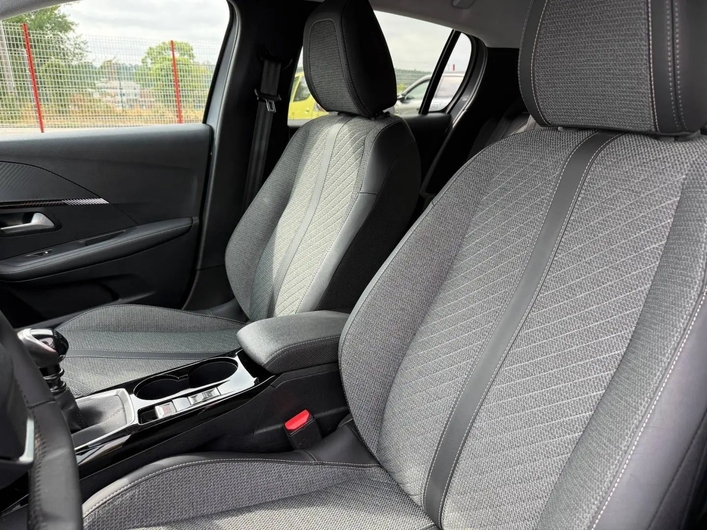 Vue intérieure côté avant droit des sièges tissu gris avec surpiqûres et accoudoir central de la Peugeot 208 1.2 100ch 2025.