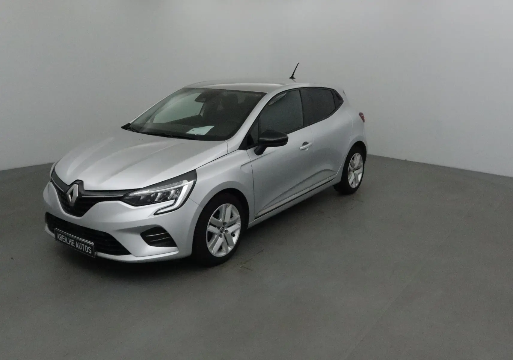 Renault Clio V gris platine vue 3/4 avant droit dans un studio, avec phares LED et jantes alliage.