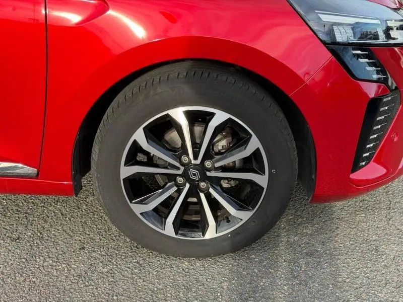 Gros plan sur la roue avant gauche et partie du bouclier rouge flamme de la Renault Clio 2025 avec jante alu noire et argent.
