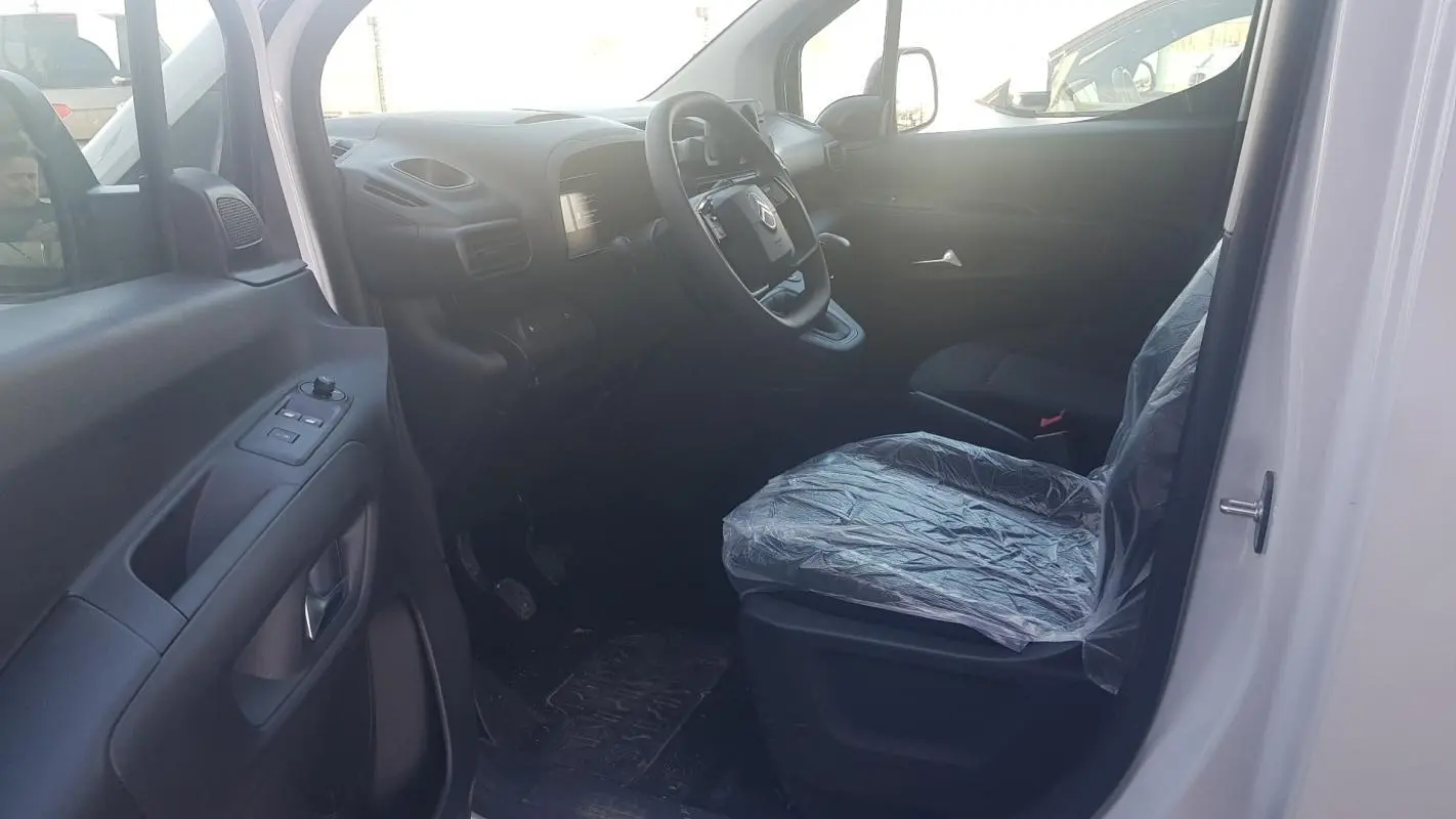 Vue intérieure côté conducteur du Citroën Berlingo blanc 2025, volant multifonctions et siège protégé par housse plastique.