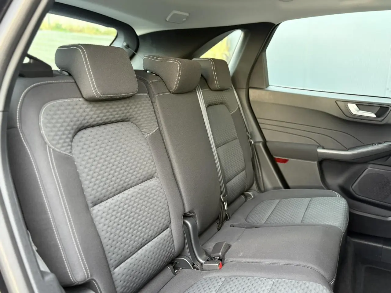 Vue latérale droite sur les sièges arrière gris texturés du Ford Kuga 2024, avec appuie-têtes et ceinture de sécurité visibles.