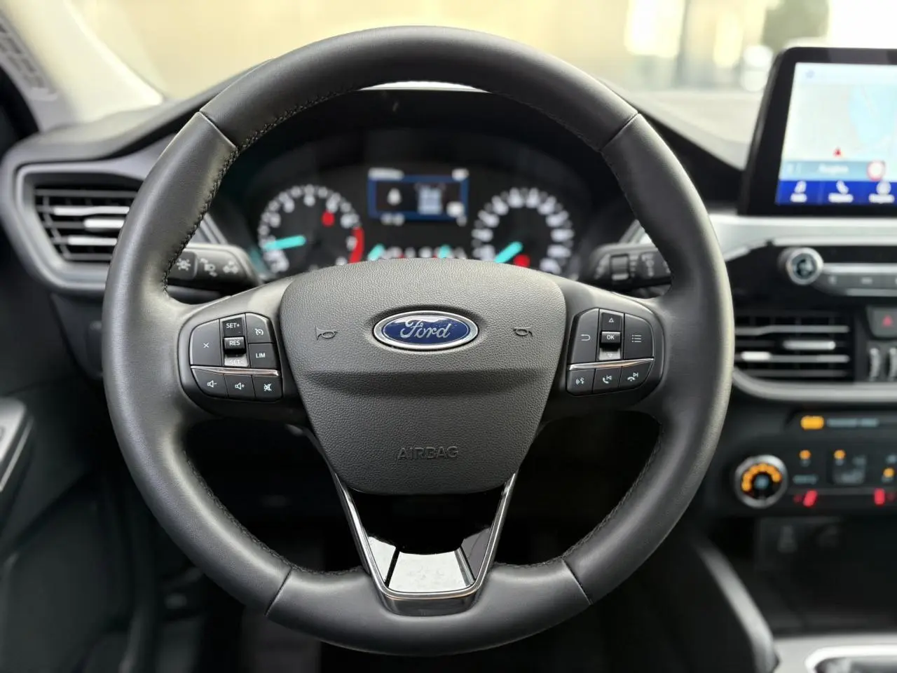 Vue rapprochée du volant en cuir noir du Ford Kuga 2024 avec commandes multifonctions et tableau de bord numérique flou.