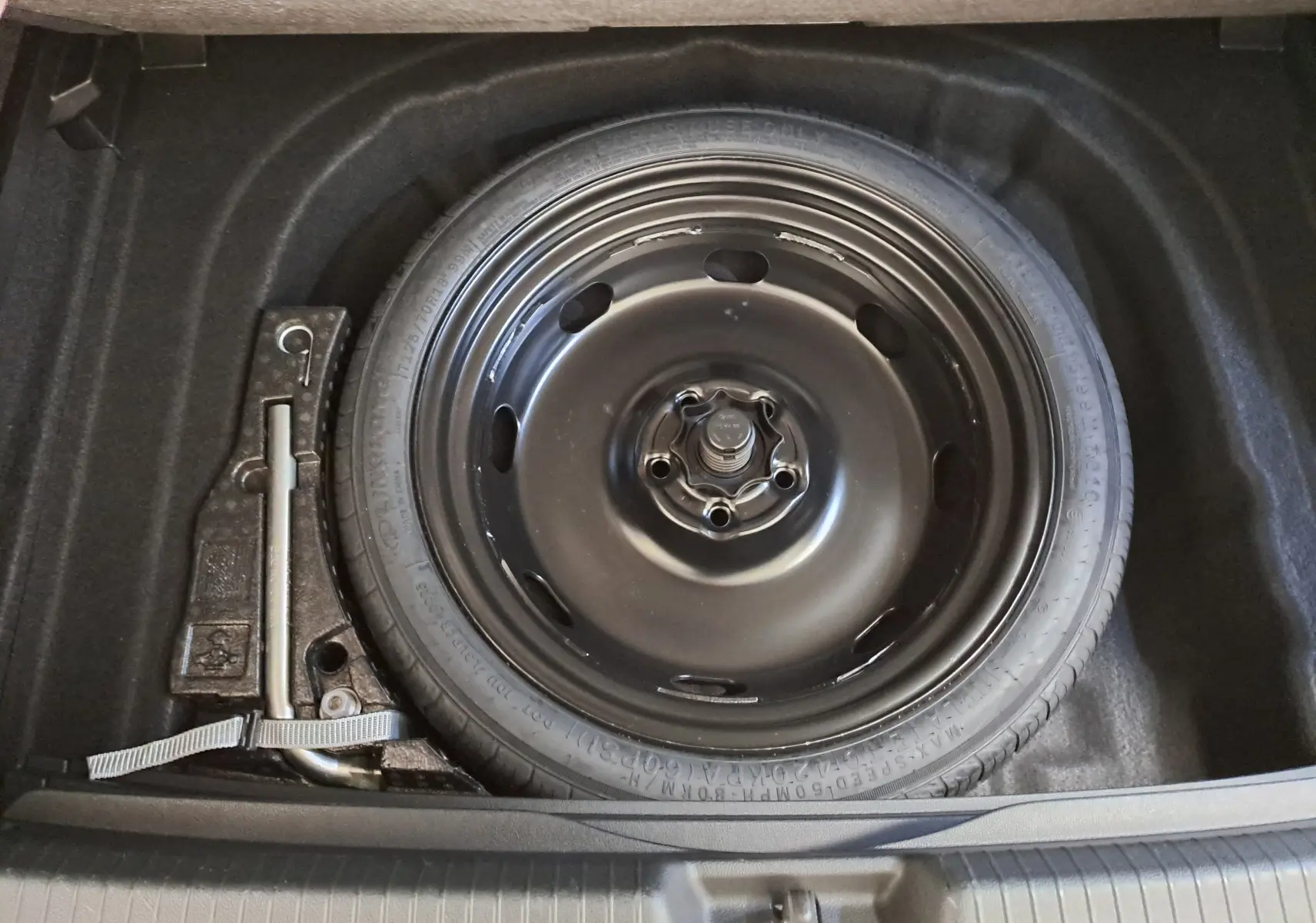 Roue de secours en acier noir avec clé de roue, vue de dessus dans le coffre d'une Volkswagen Golf 2025.