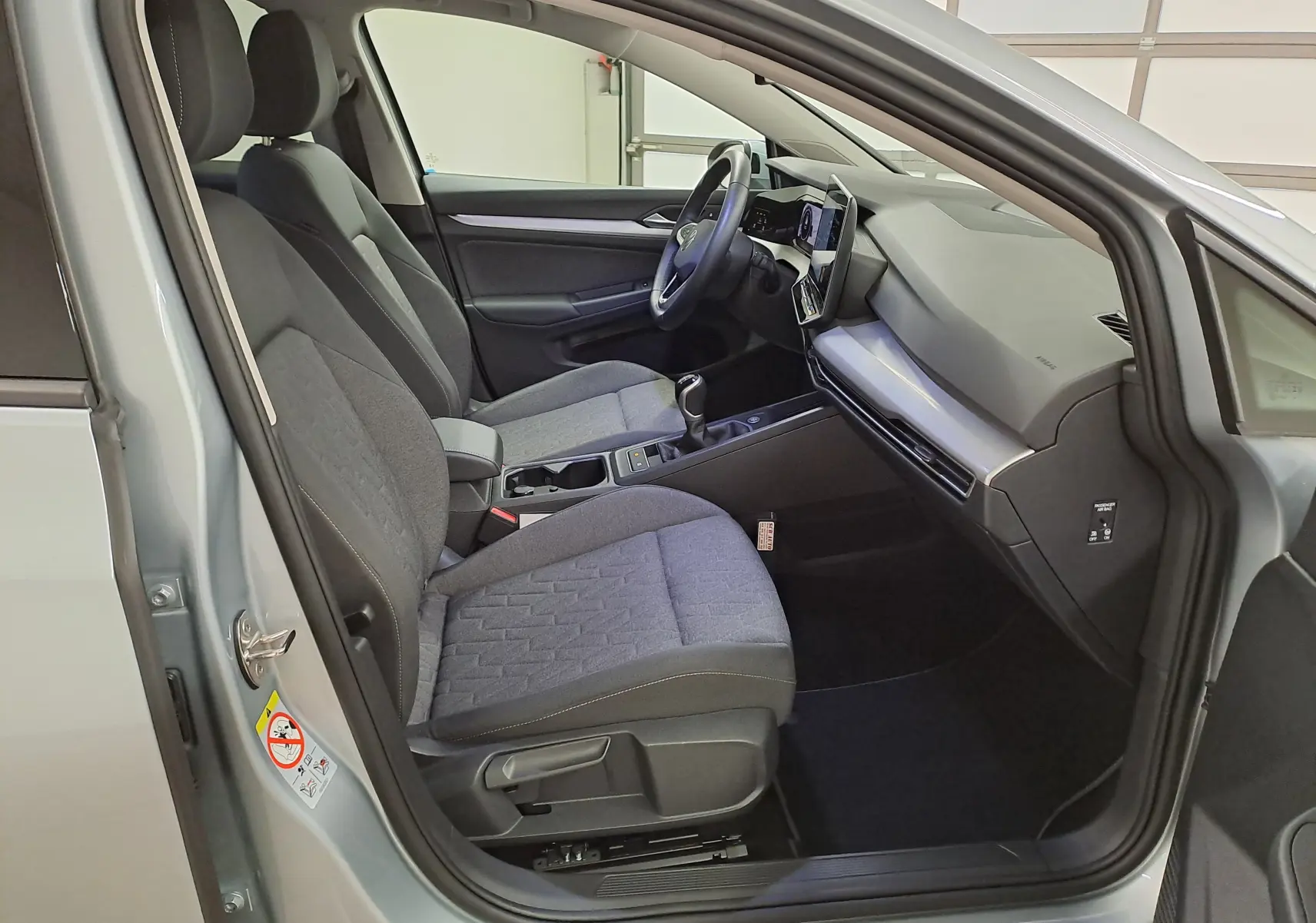 Vue intérieure côté conducteur d'une Volkswagen Golf 1.5 eTSI 116 BVM6 argent Dolomite, avec sièges tissu gris et tableau de bord moderne.