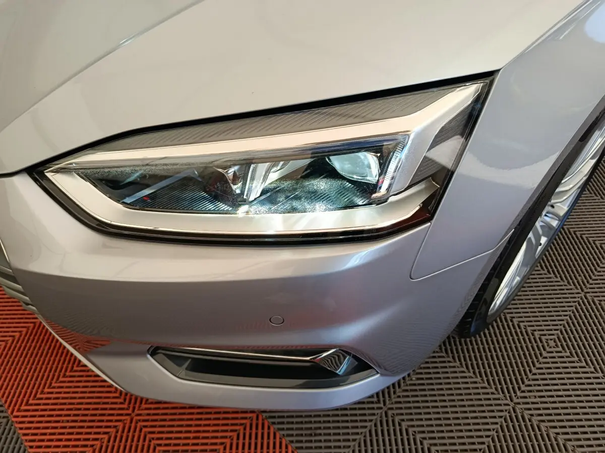 Gros plan sur le phare avant droit d'une Audi A5 gris clair, mettant en valeur les lignes nettes et les détails LED.