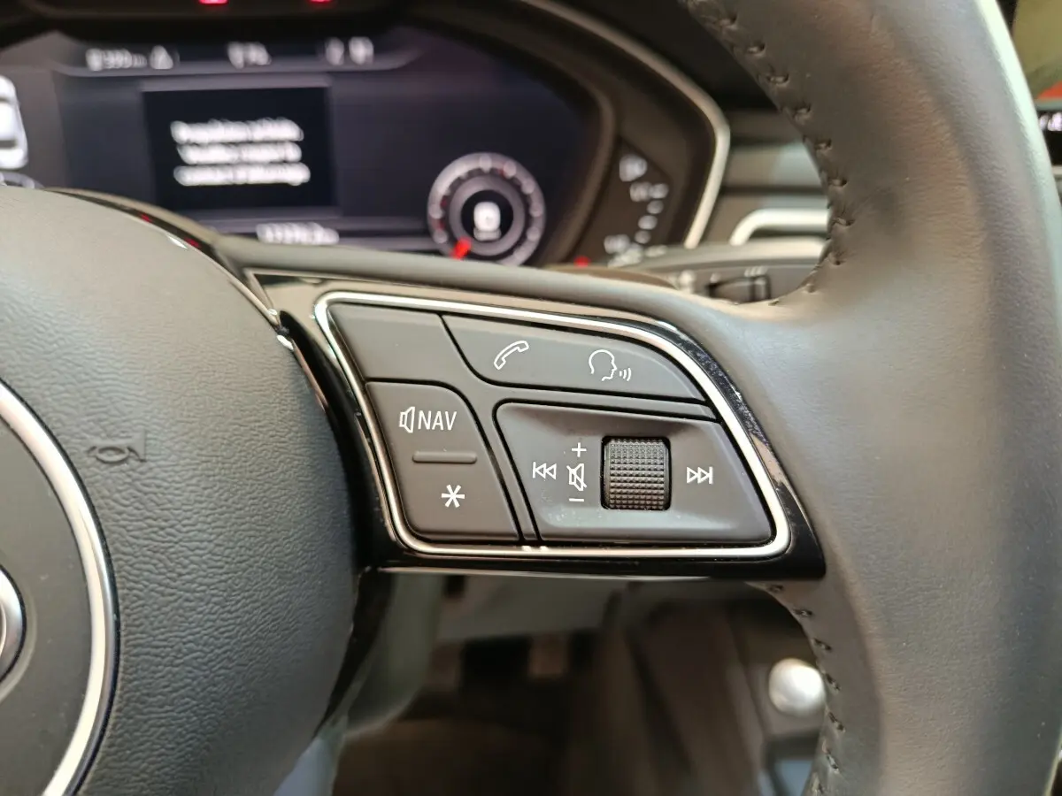 Gros plan sur les commandes multimédias au volant cuir noir d'une Audi A5 gris clair, tableau de bord flou en arrière-plan.