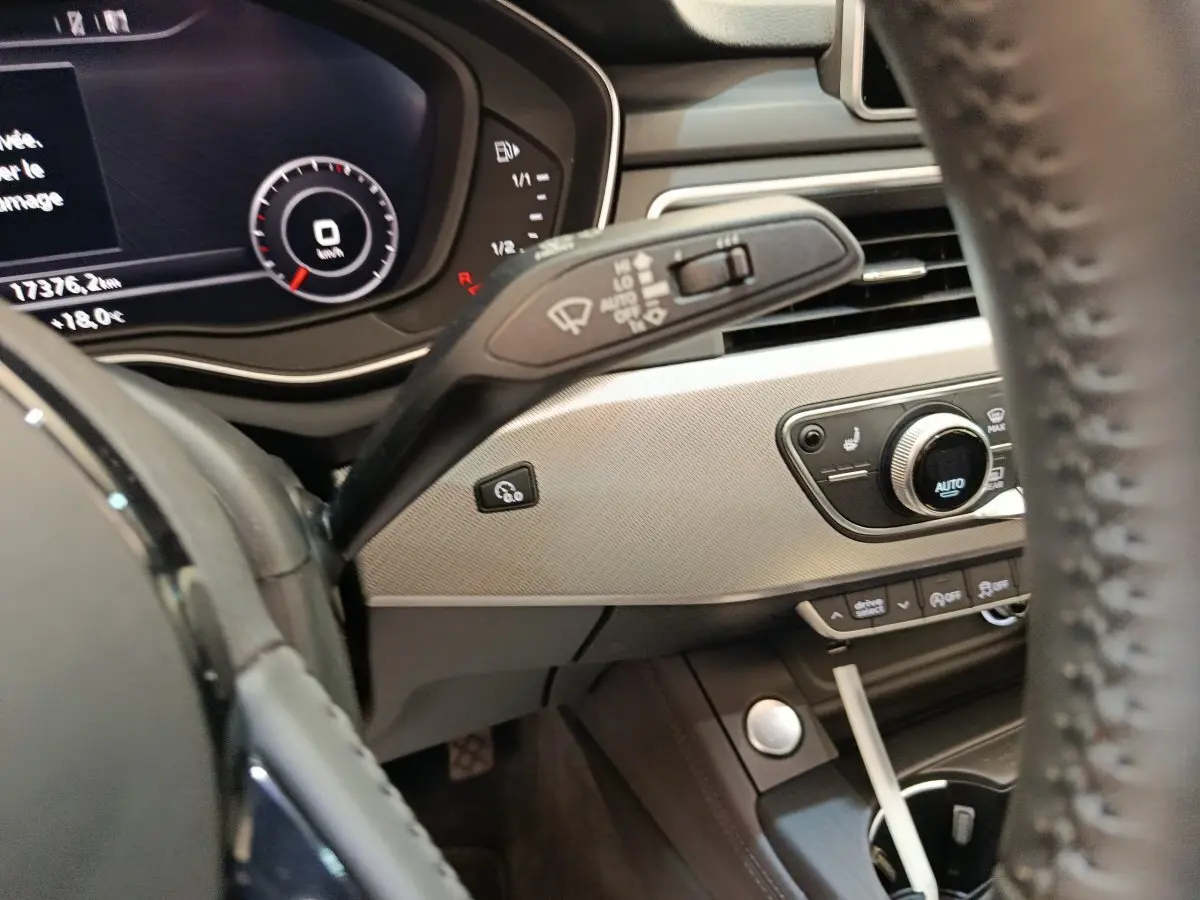 Vue intérieure côté conducteur de l'Audi A5 gris clair, avec tableau de bord digital et commandes de climatisation visibles.