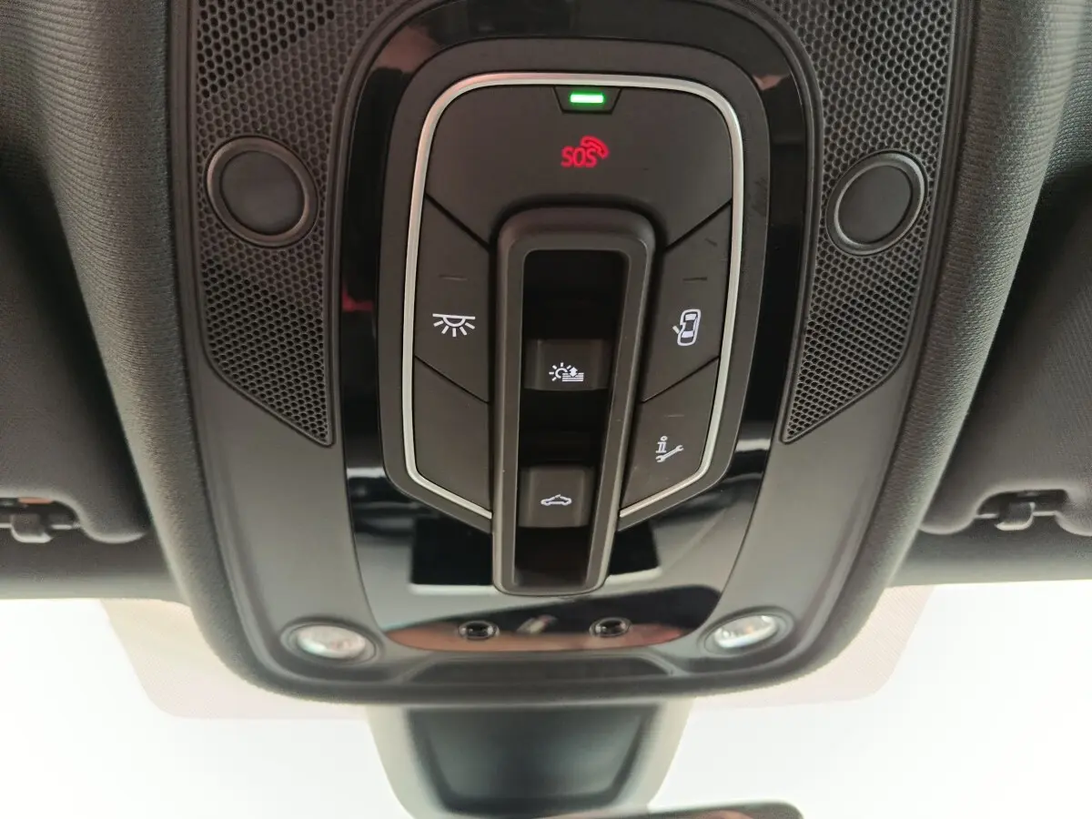 Vue en contre-plongée du panneau de commandes de toit intérieur noir avec boutons d’éclairage et SOS sur Audi A5 gris clair.