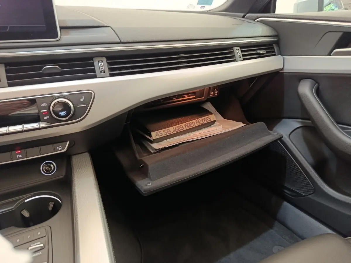 Vue intérieure côté passager de l'Audi A5 2019, boîte à gants ouverte avec documents visibles, tableau de bord gris clair.