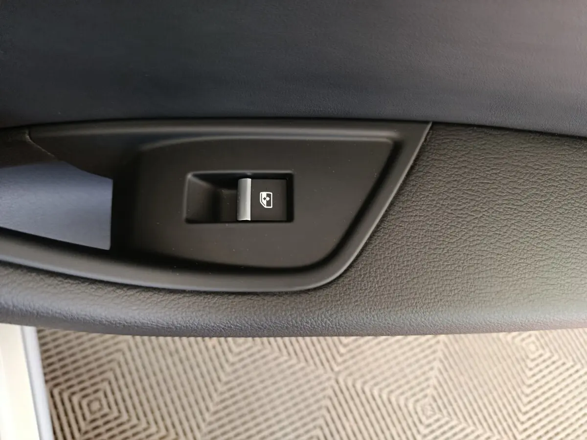 Gros plan sur le bouton de commande de la vitre électrique, sur la porte intérieure noire de l'Audi A5 gris clair.